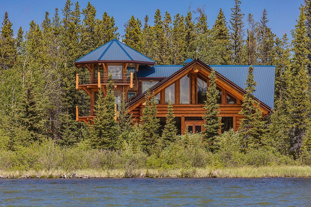 A large log cabin sits on the shore of Chilko Lake, Canada surrounded by trees.