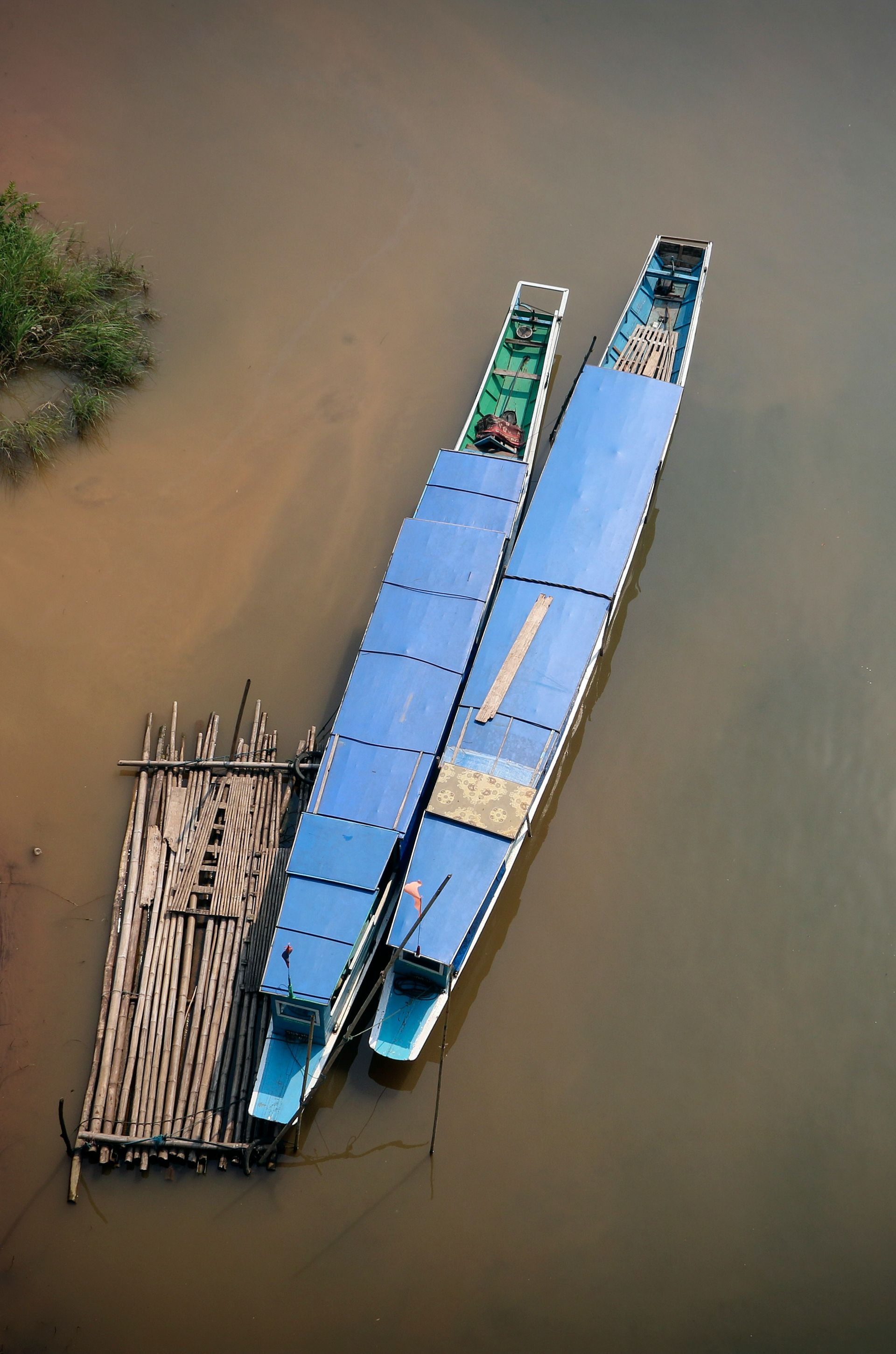 Two blue boats docked on brown water next to a wooden dock in Nong Khiaw, Laos.