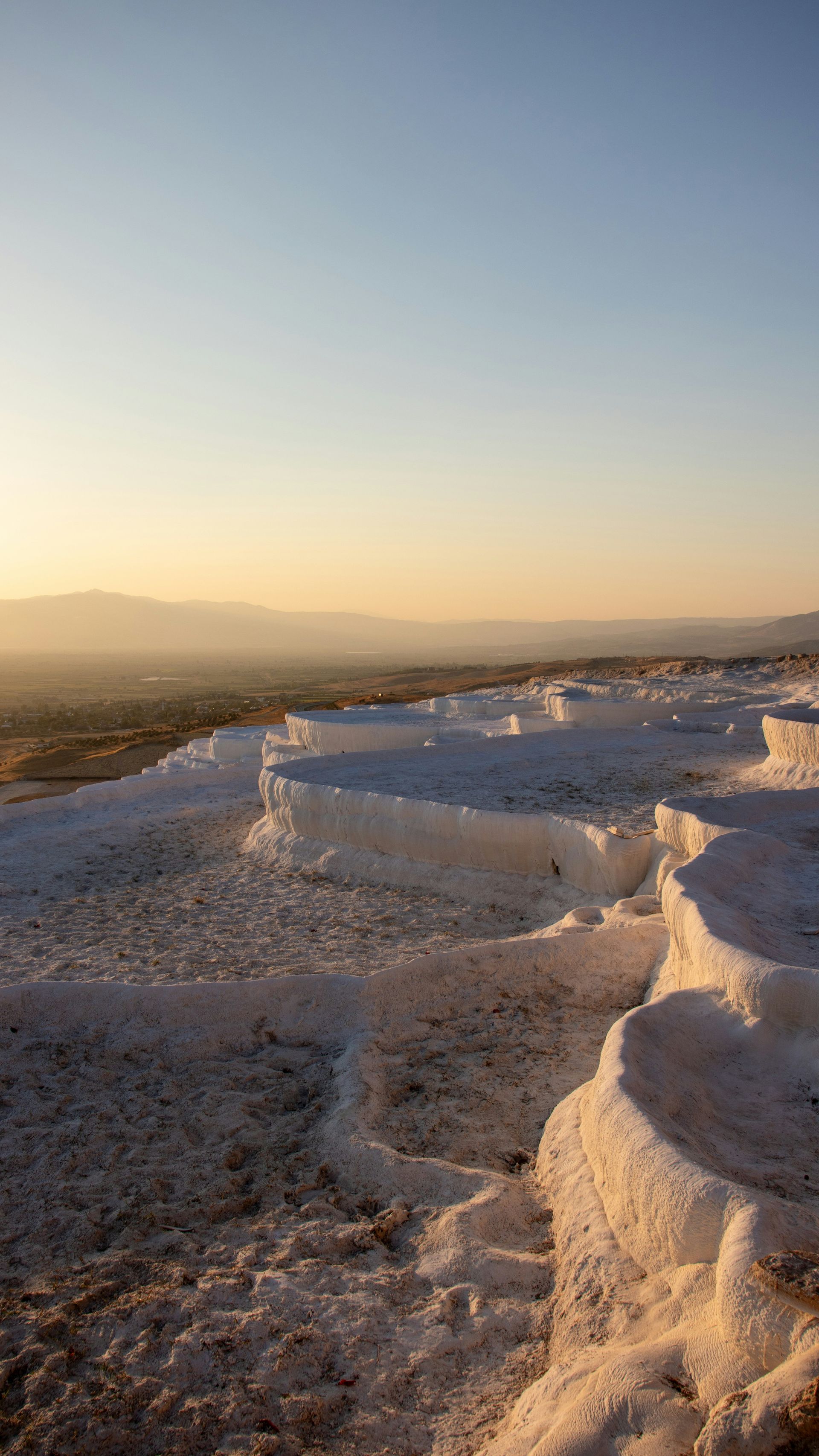 White, terraced travertine pools in Pamukkale, Turkey, with a golden sunset sky in the background.