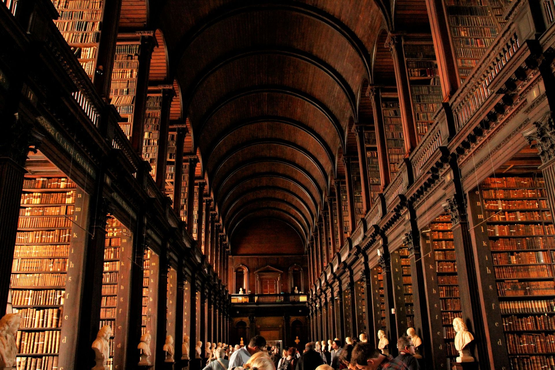 Long, dark library interior with arched ceiling, filled with books and people at Trinity College, Dublin.