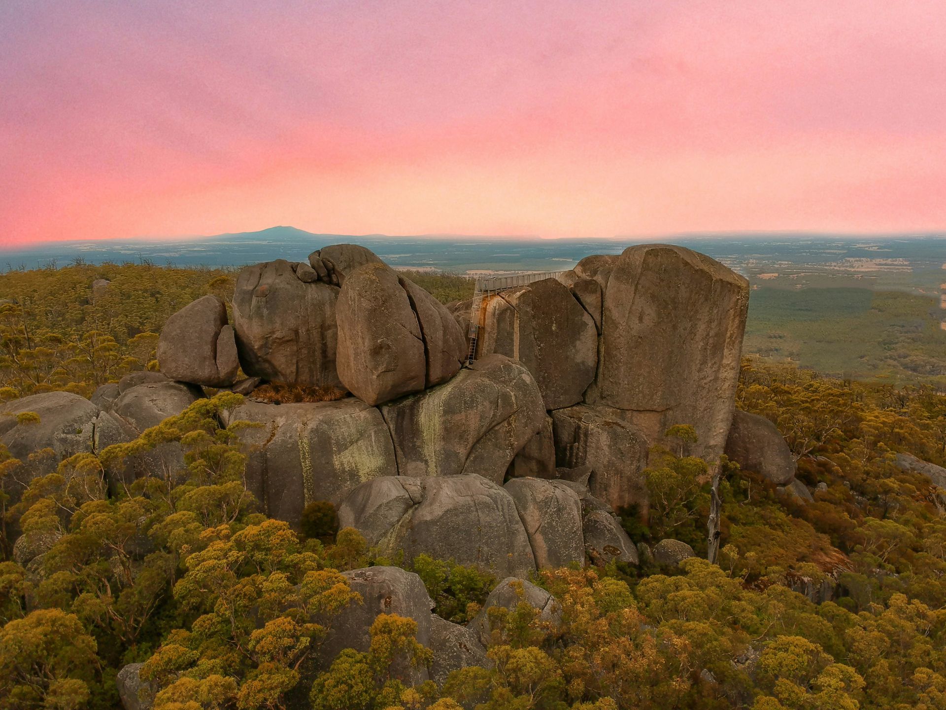 A large rock formation in the middle of a forest with a sunset in the background in Western Australia.