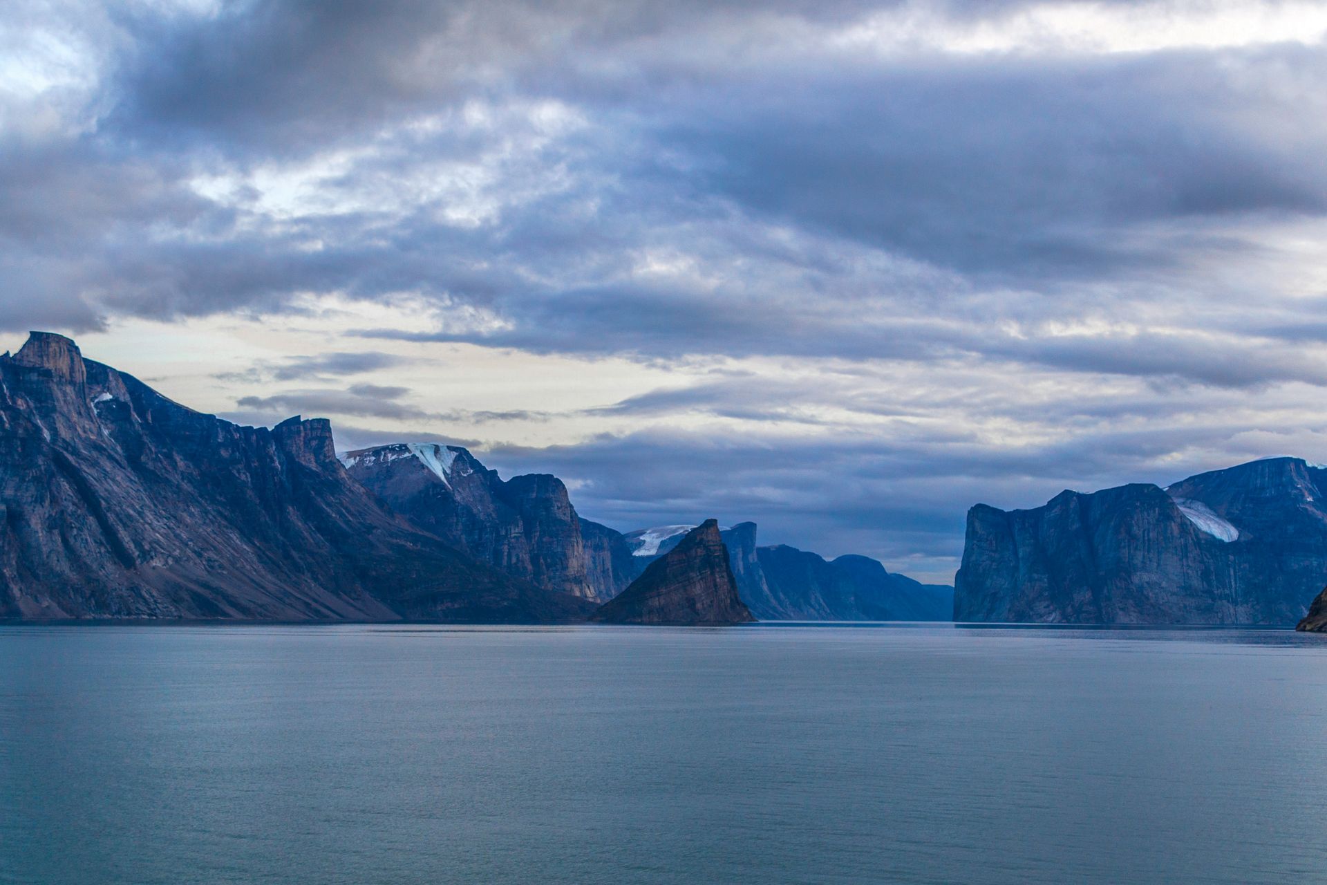 Mountains frame a misty ocean under a cloudy sky, surrounded by rugged, dark peaks in the Northwest Passage, Canada.