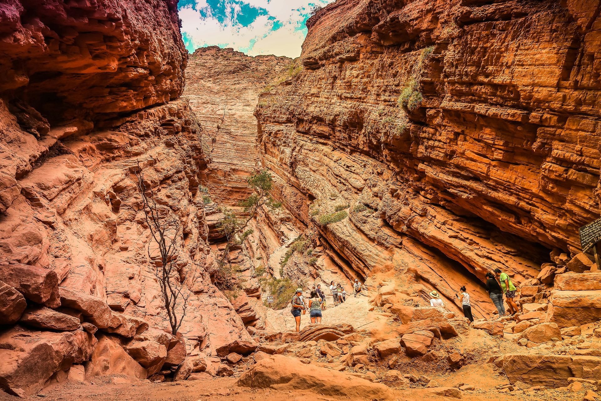 People hiking through a narrow canyon with red rock walls in Salta, Argentina.