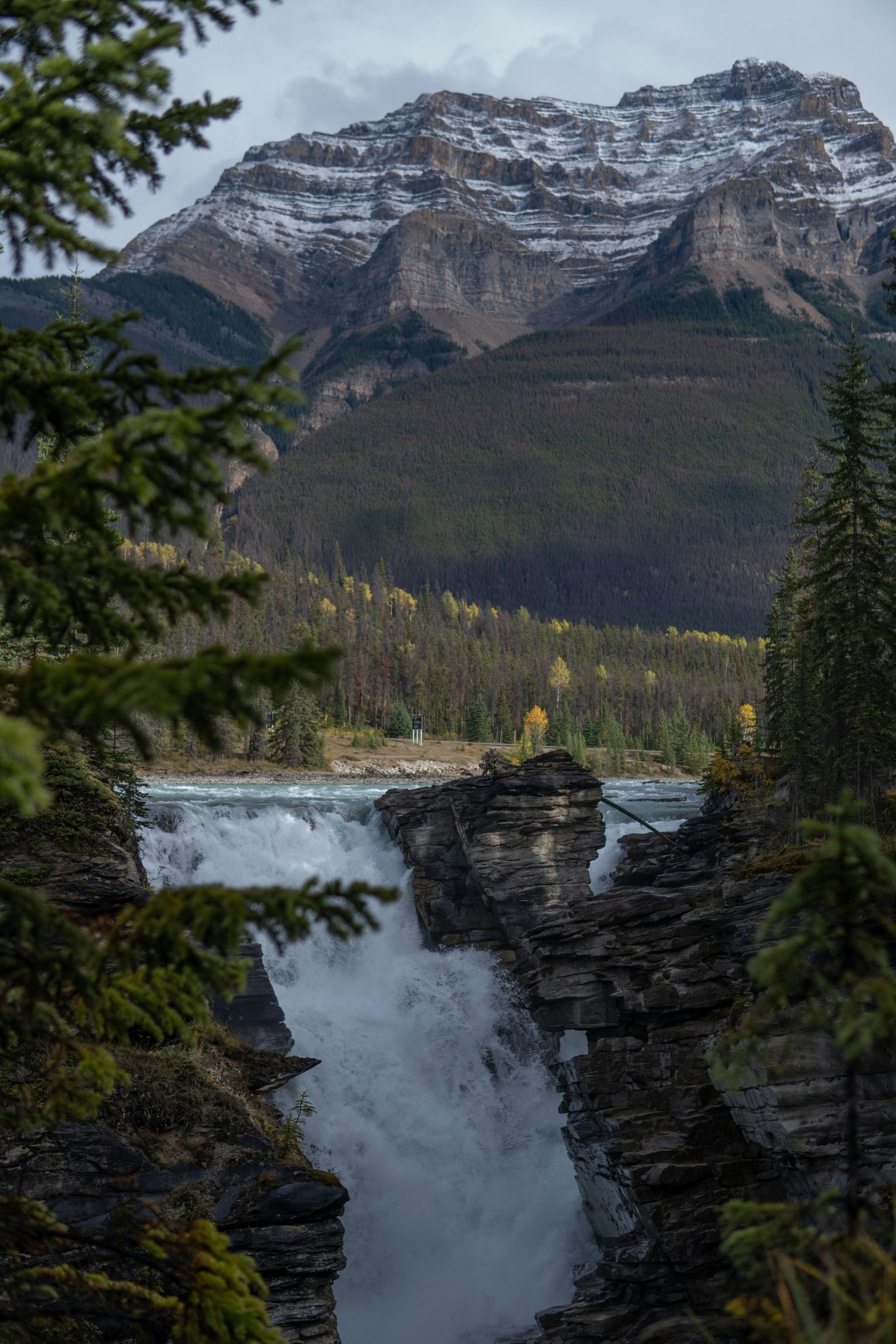 Waterfall cascading over rocky cliffs, with a snow-capped mountain in the background, in Jasper, Canada.