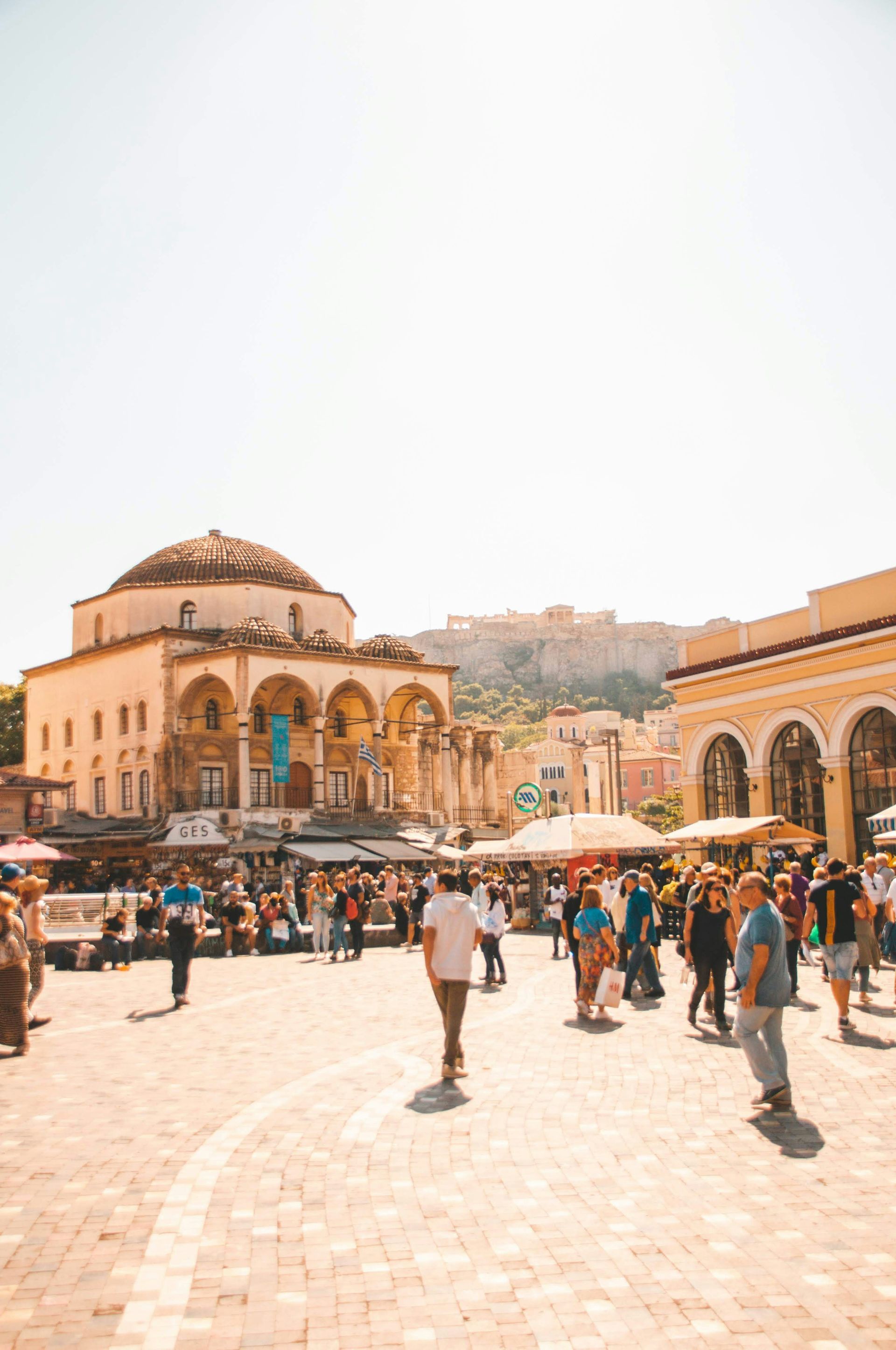 A group of people are walking down a brick street in front of a building in Athens, Greece.