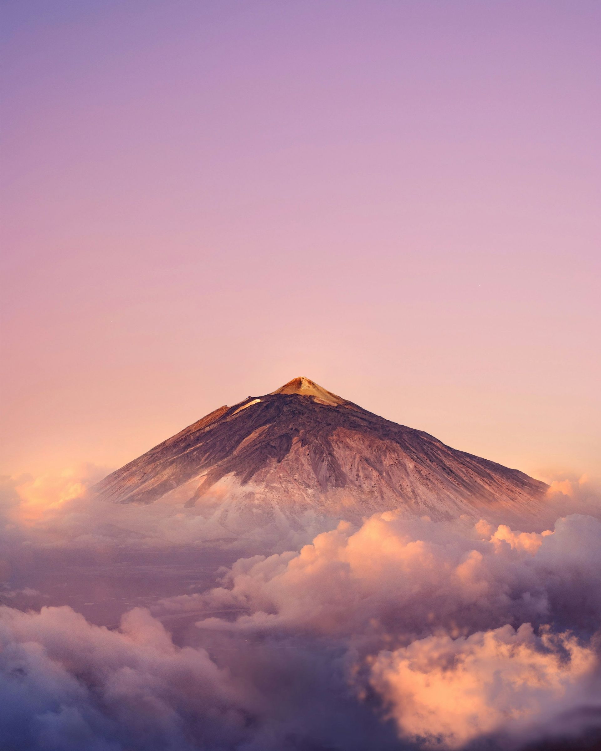 Volcano peak piercing through soft, lavender-colored clouds, illuminated by warm light on the Canary Islands, Spain.
