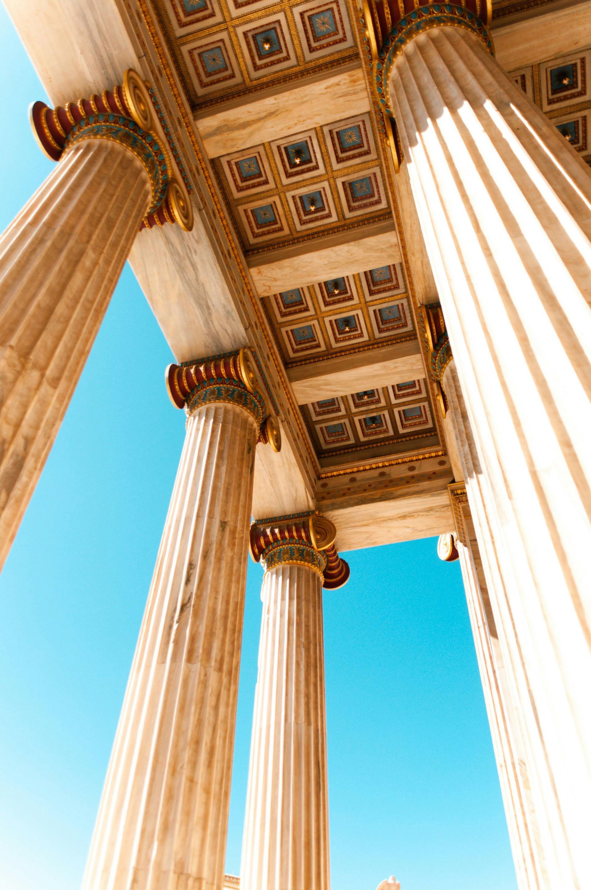 Looking up at the columns of a building with a blue sky in the background in Athens, Greece.