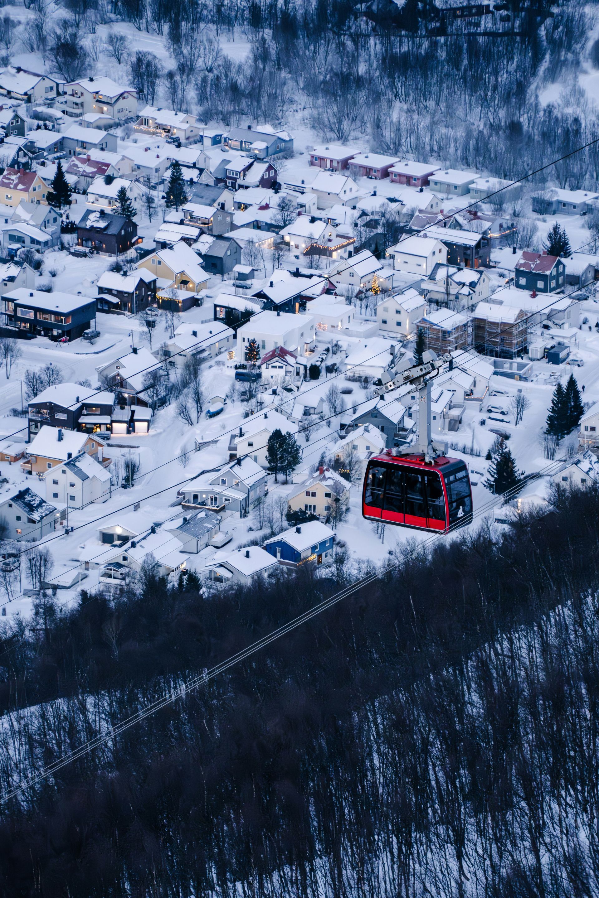 Red cable car descending toward the snow-covered village of Tromsø, Norway nestled in a wintry mountain setting.