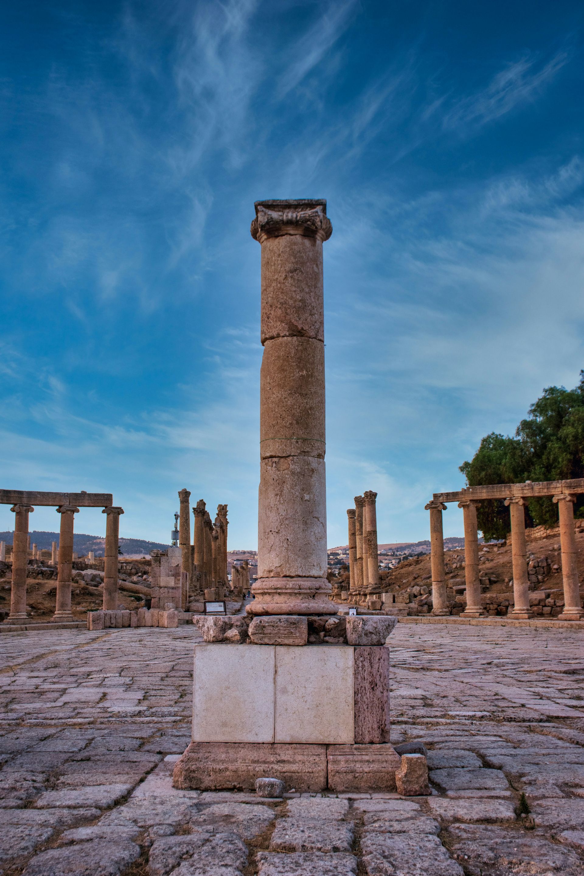 Ancient Roman column in ruins under a blue and cloudy sky in Jerash, Jordan.