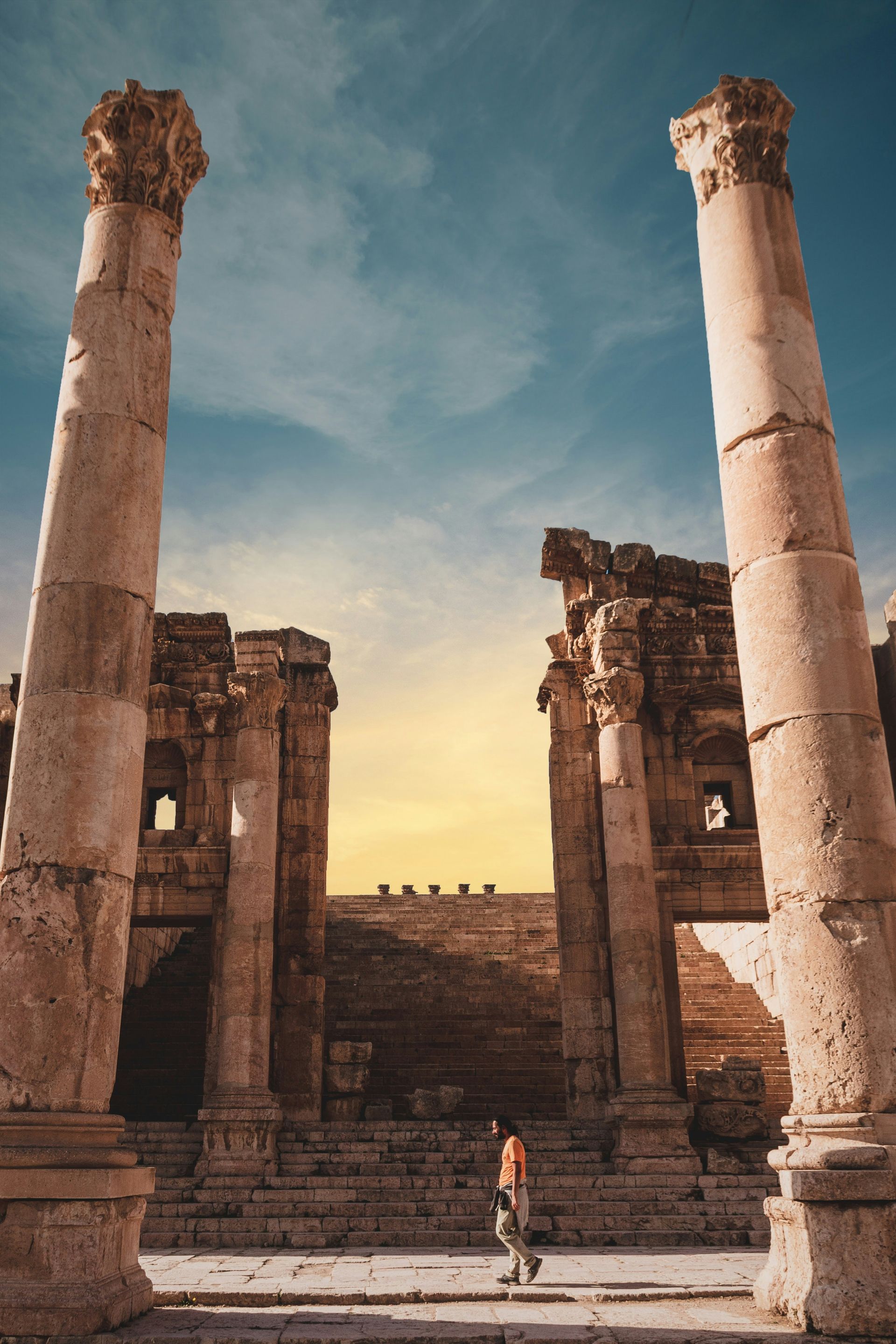 Ancient Roman ruins with tall columns; person walks through the archway in Jerash, Jordan.