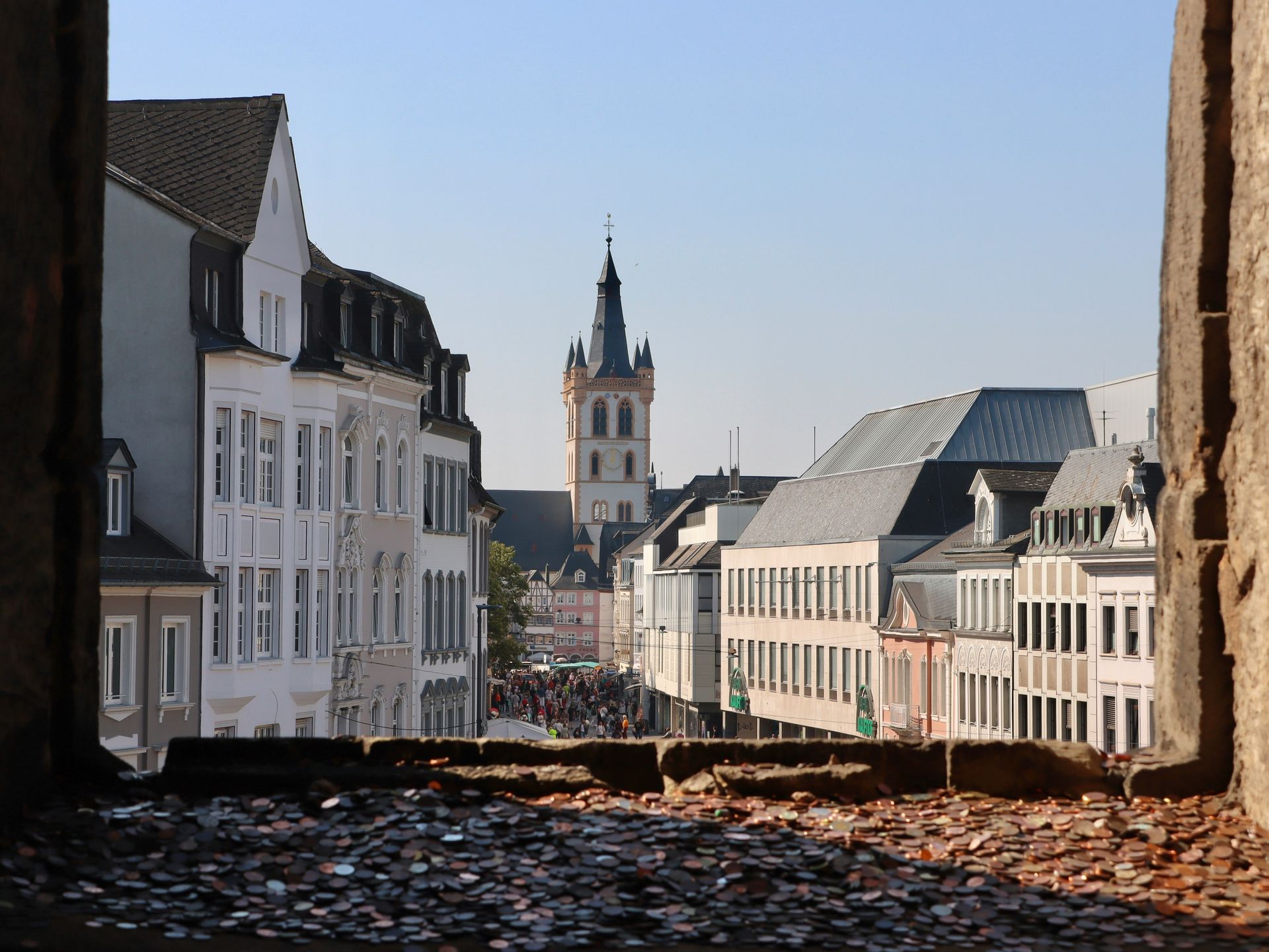 View of street with buildings and a church tower. Seen from a stone opening, with sunlight in Trier, Germany.