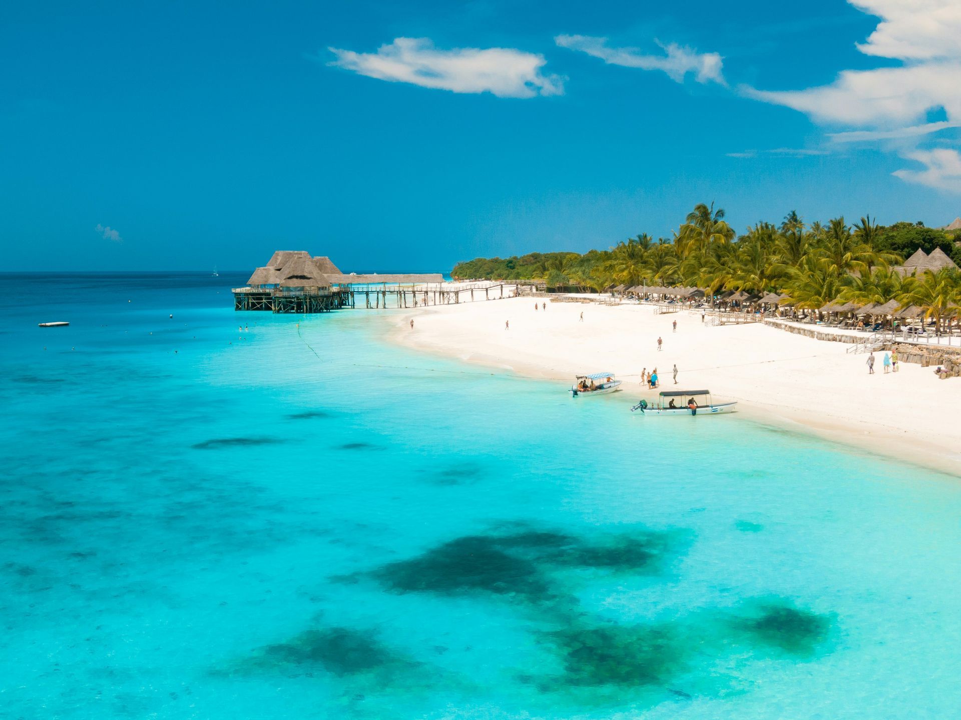 An aerial view of a tropical beach with a pier in the background in Zanzibar, Tanzania.