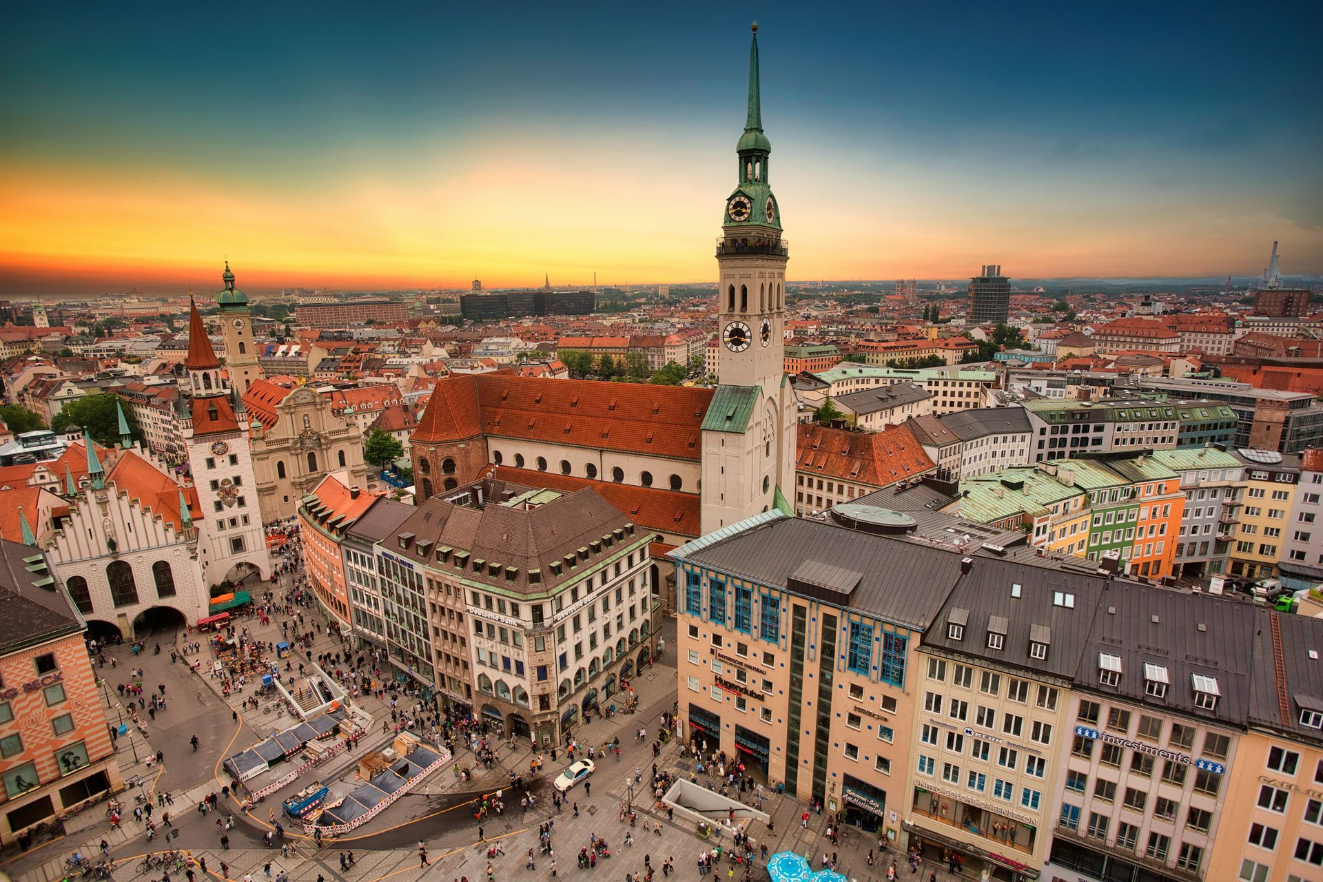 Aerial view of Munich, Germany, with iconic architecture and crowded square at sunset.