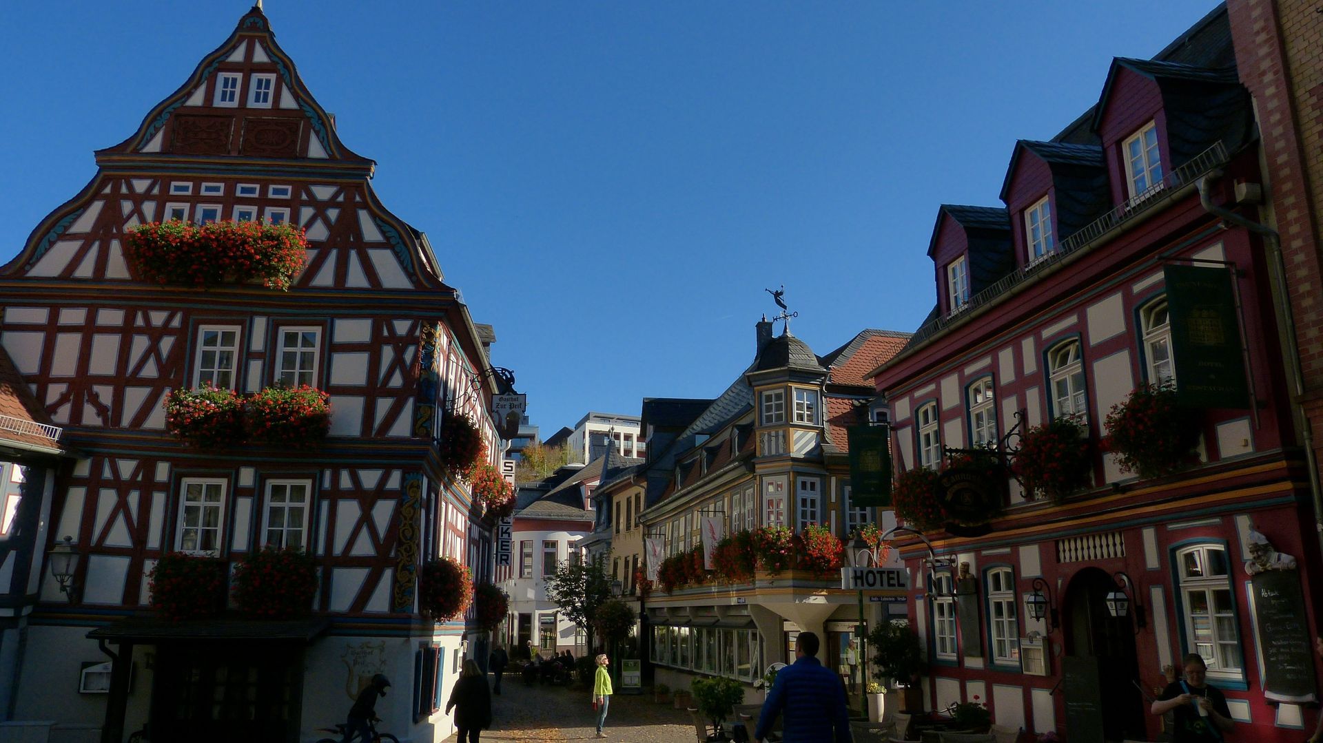 A group of people are walking down a street between two buildings in Idstein, Germany.