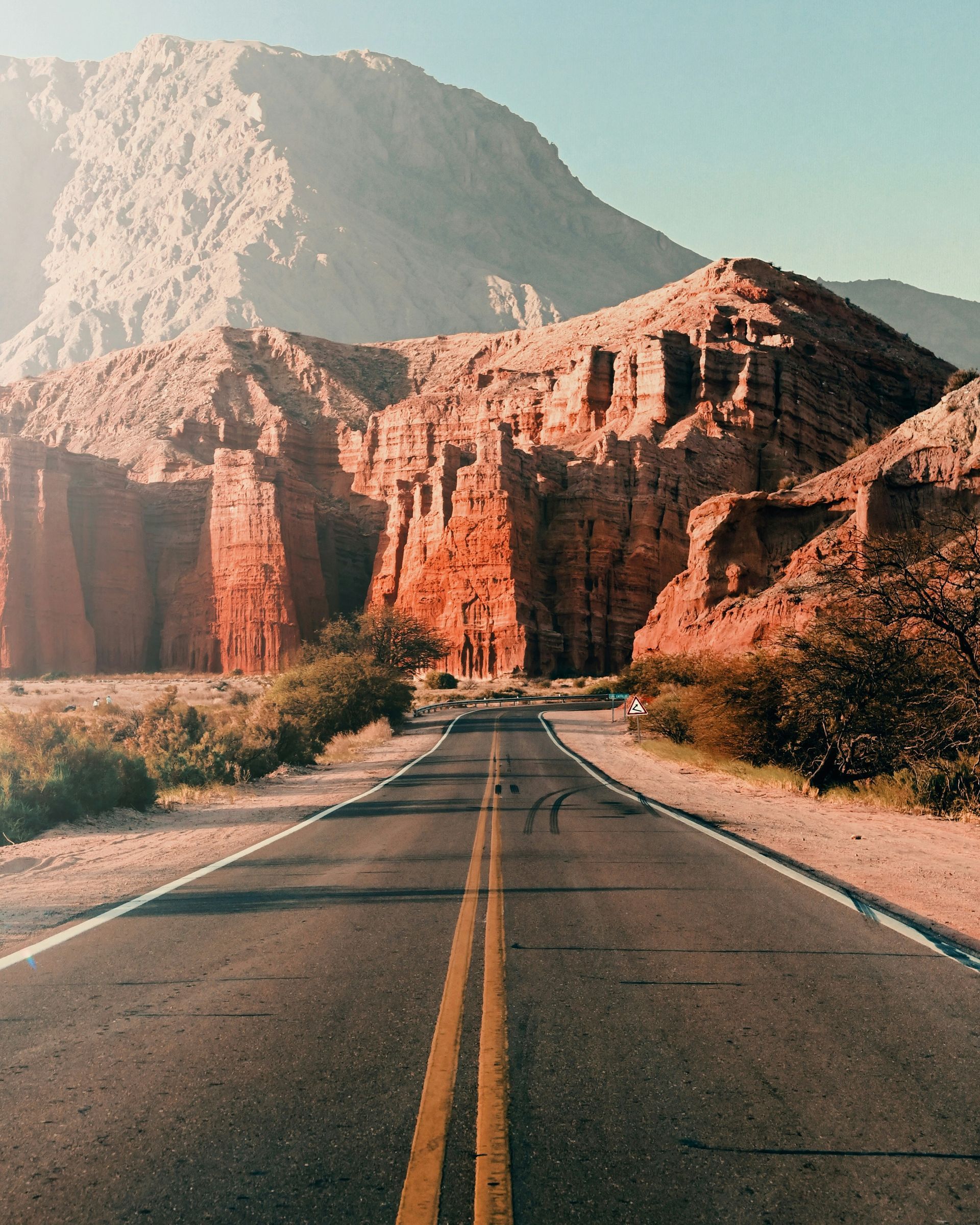 Road through red rock canyons under a hazy sky in Salta, Argentina.