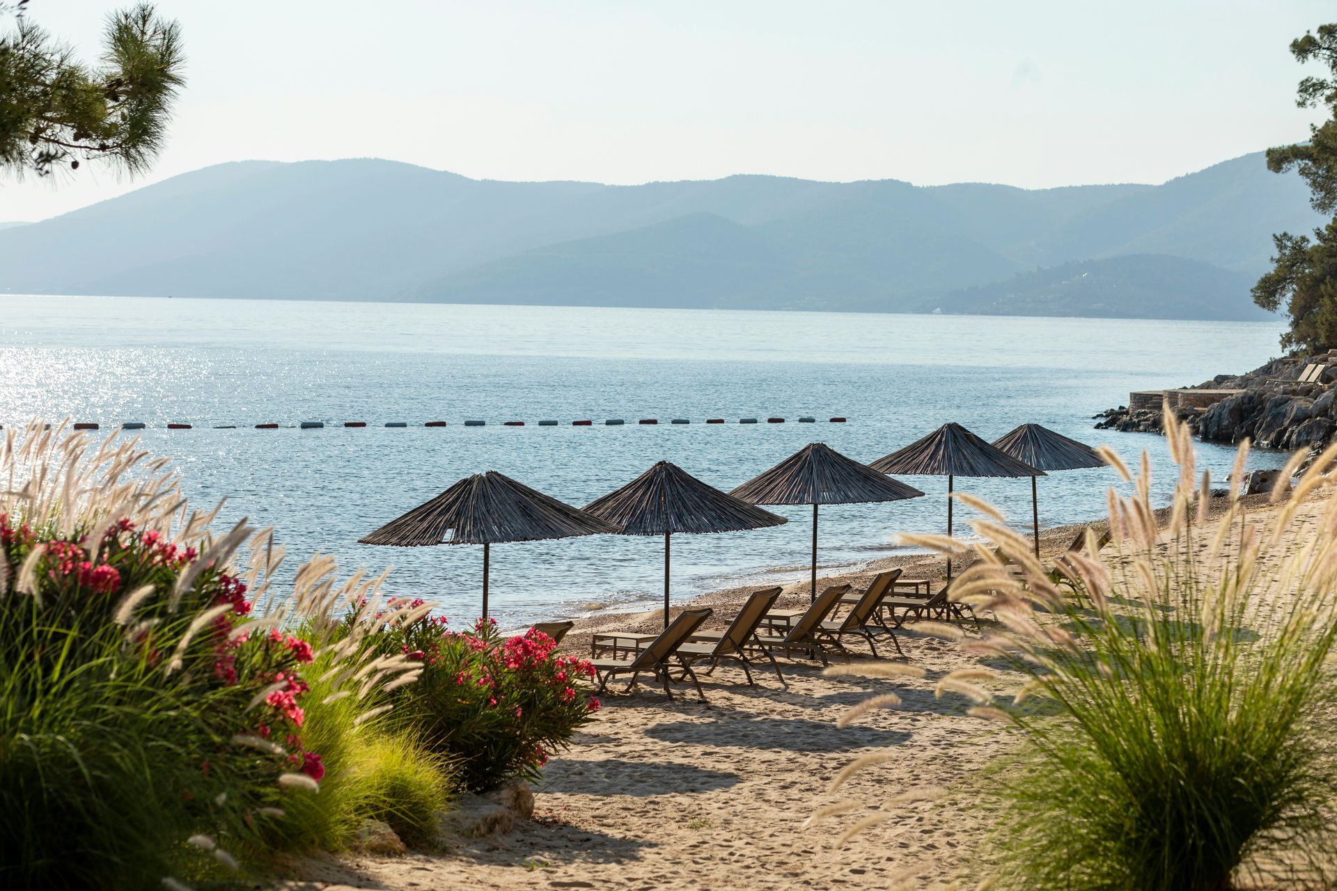 Beach with straw umbrellas, wooden lounge chairs, and calm blue water in Bodrum, Turkey.