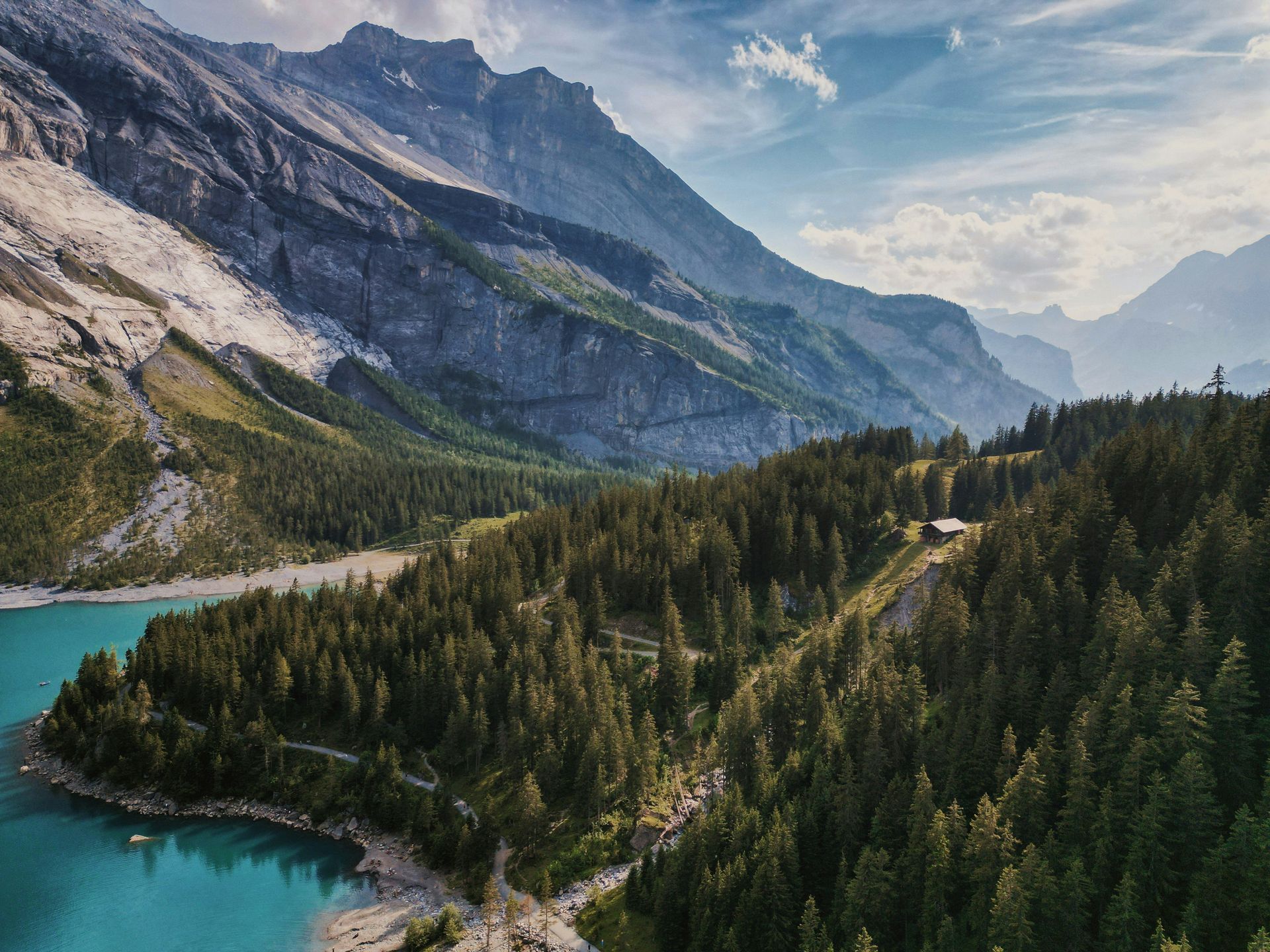 Mountainous landscape with the turquoise Lake Oeschinensee, evergreen forest, and a small cabin in Kandersteg, Switzerland.