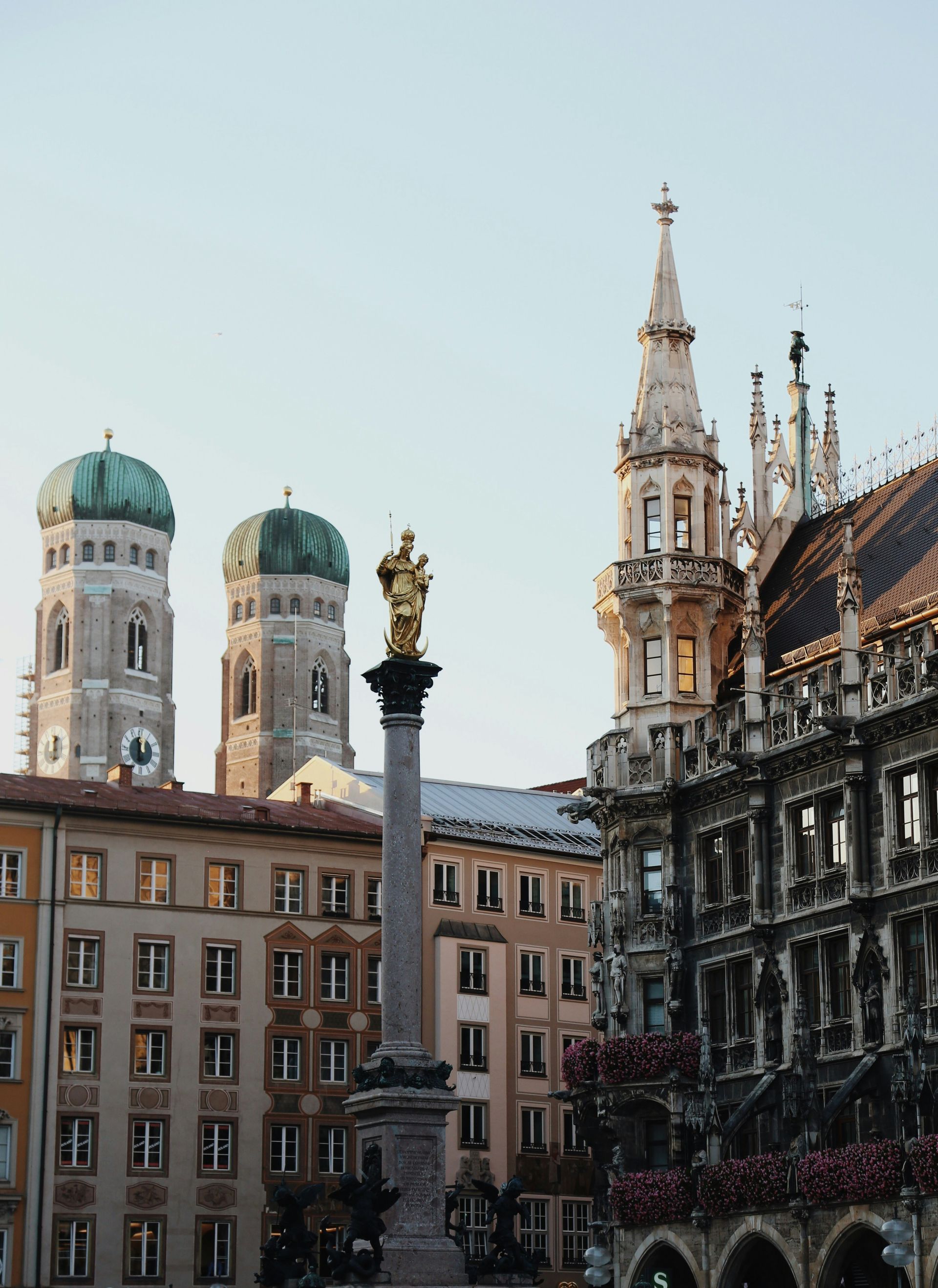 A cityscape in Munich, Germany. Features the Frauenkirche towers, a column, and the Neues Rathaus.
