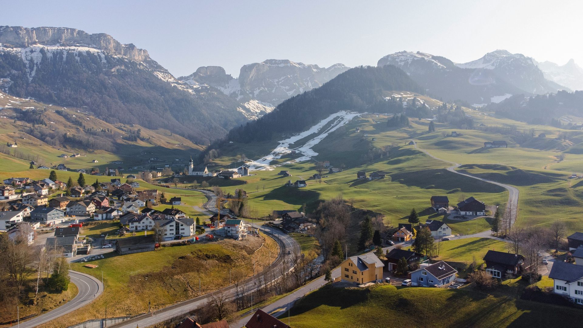 Valley village nestled between mountains, road in foreground, sunny day in Schwende, Switzerland.
