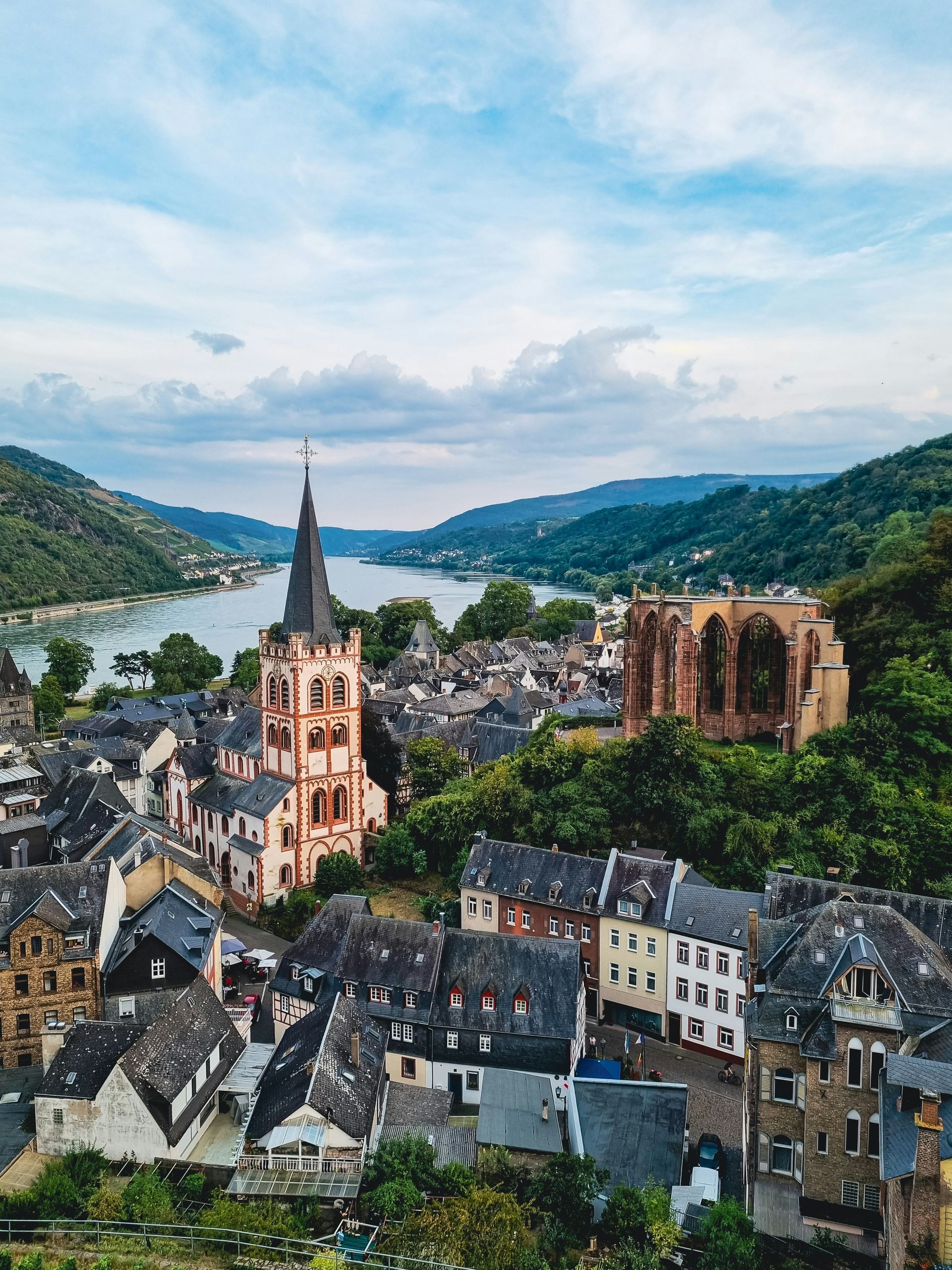 Bacharach, Germany, with a church and ruins overlooking the Rhine River Gorge, and green hills.