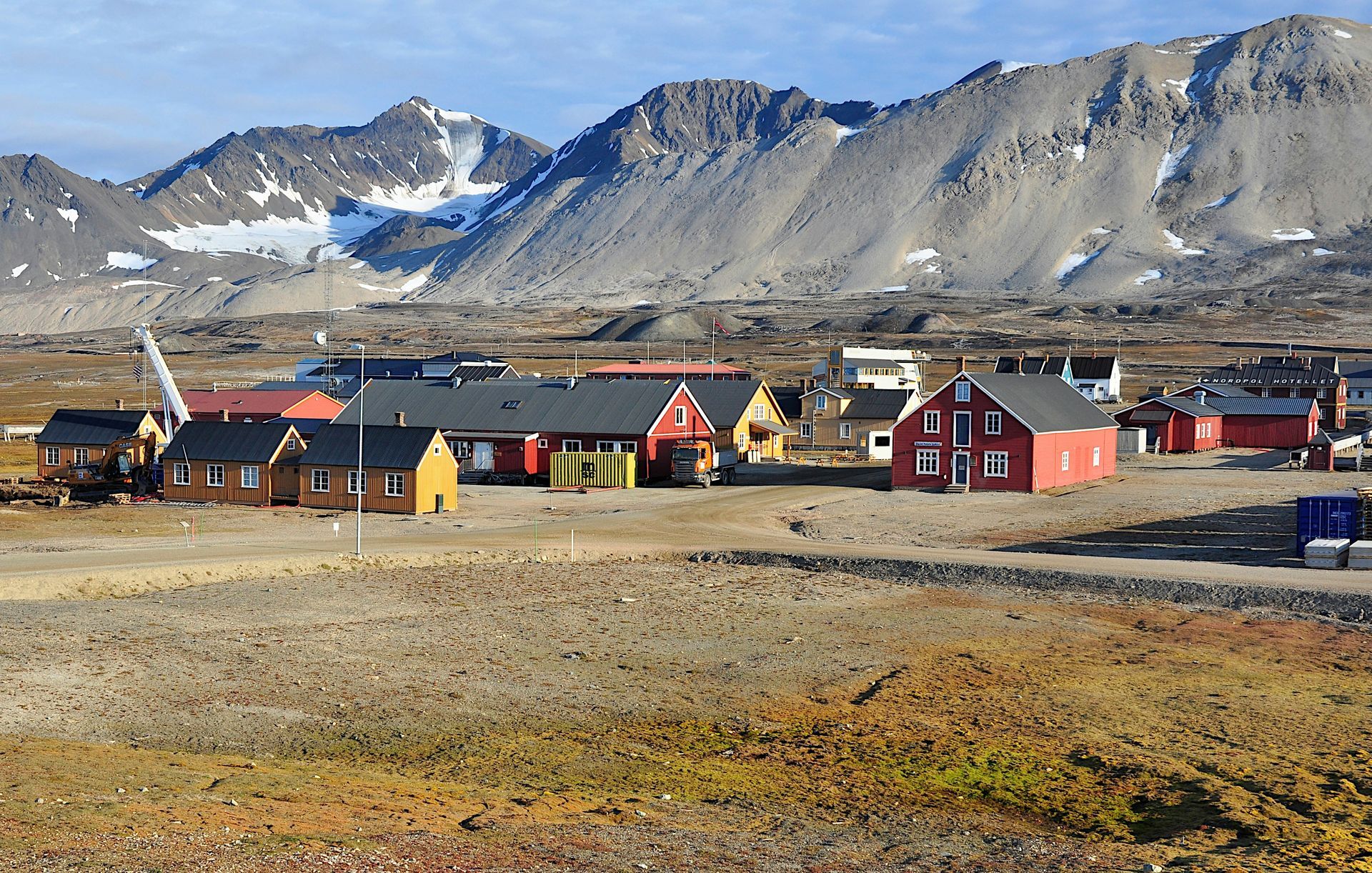 A small village with colorful buildings sits at the base of rugged mountains in Svalbard, Norway.