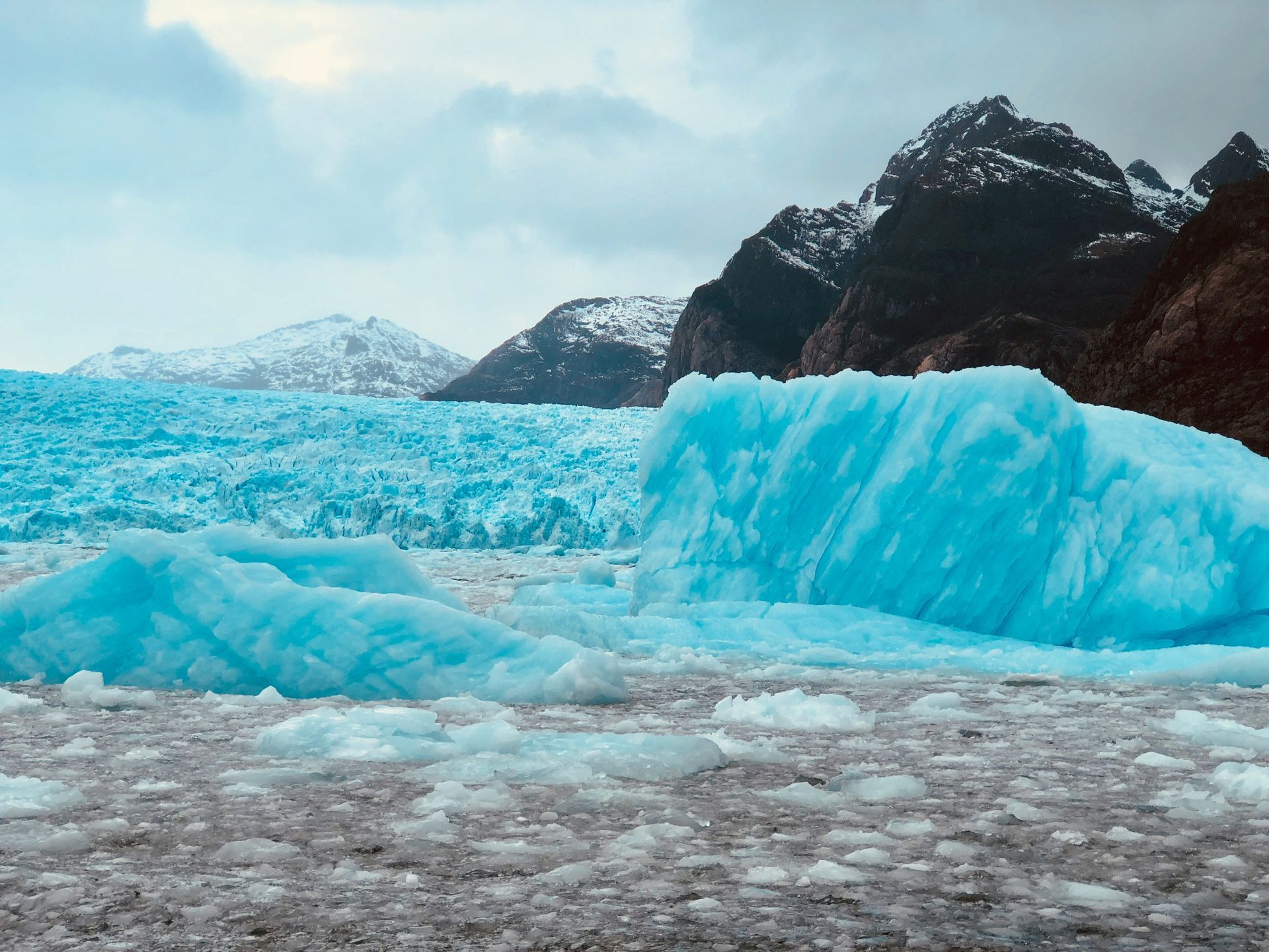 Blue glacier icebergs floating on icy water, mountains in the background in Aysén, Chile.