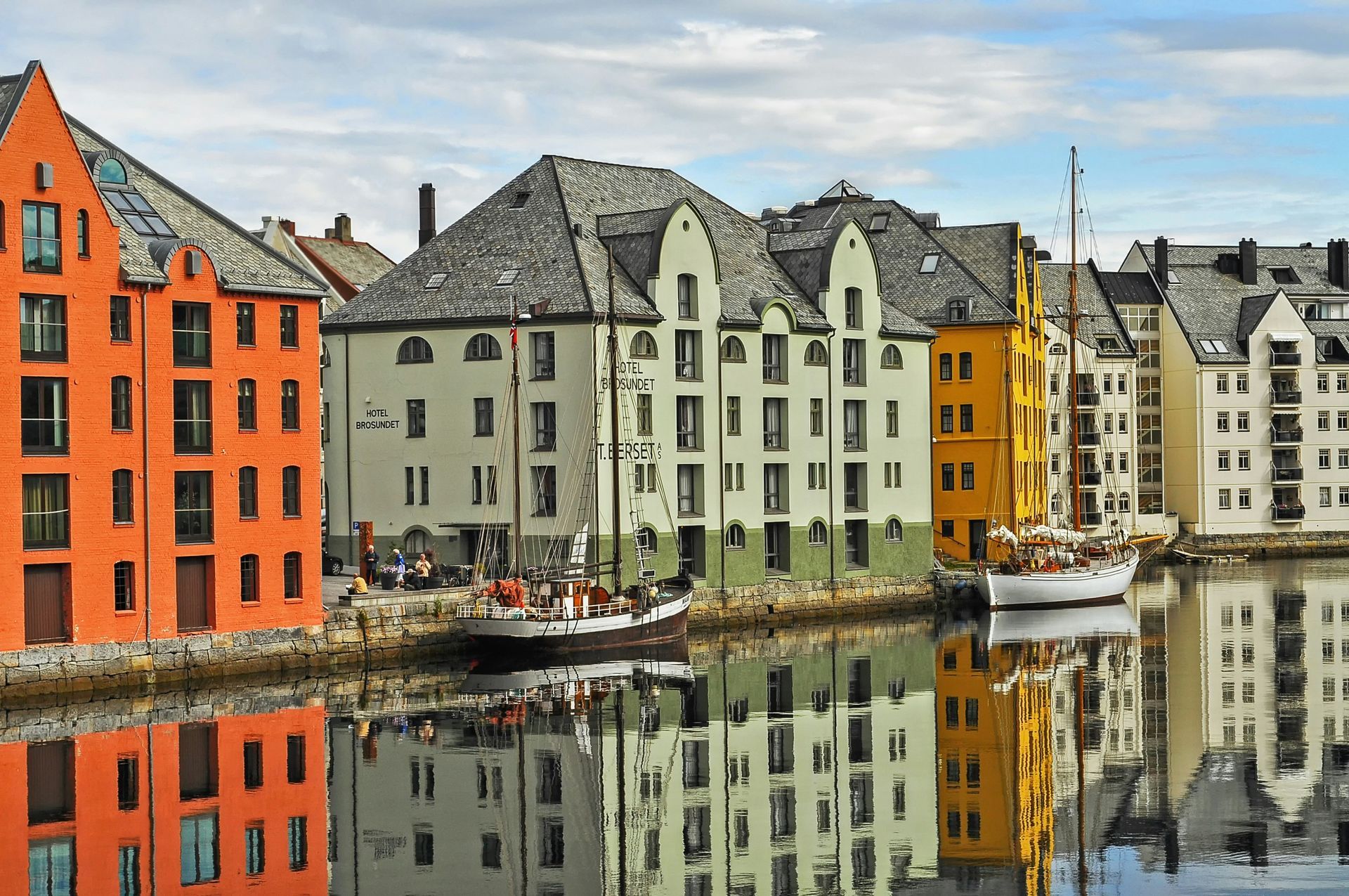 Colorful buildings line a canal in Ålesund, Norway; sailing boats reflect in the water.