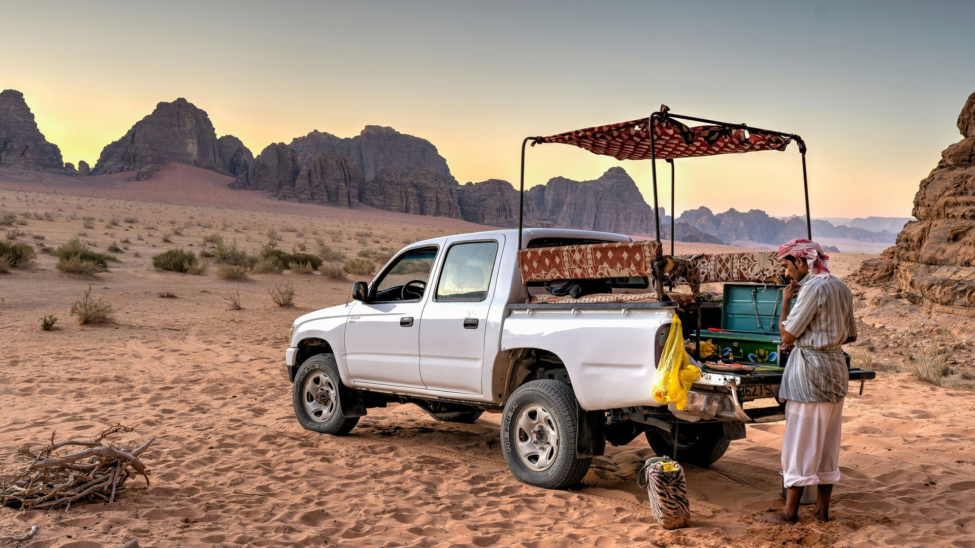 White pickup truck with canopy in Wadi Rum, Jordan; a man stands near truck, mountains in the background.