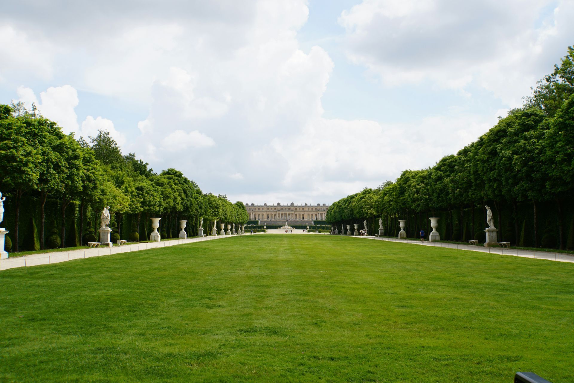 A large grassy field with a large building in the background at the Palace of Versailles in France.