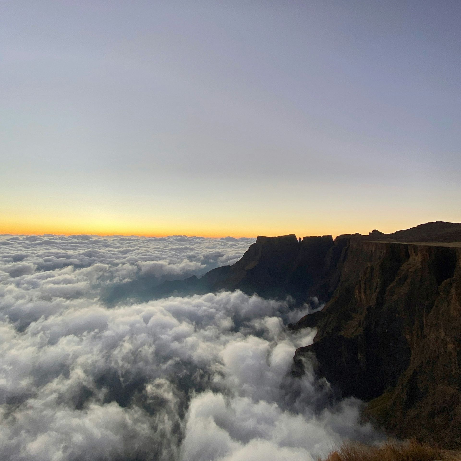 Cliffside above a sea of clouds at sunset; orange glow on horizon in the Drakensberg, South Africa.