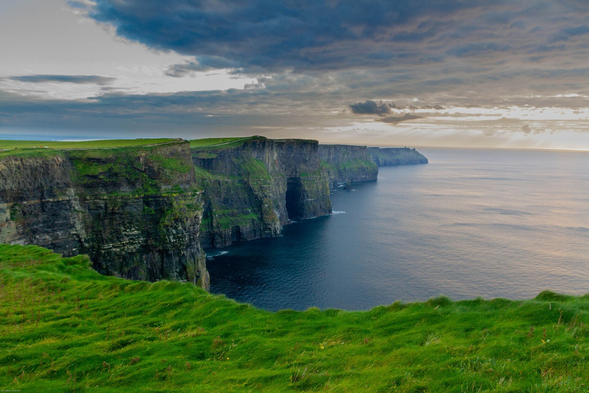 The green Cliffs of Moher meeting the dark ocean under a cloudy sky in Ireland.