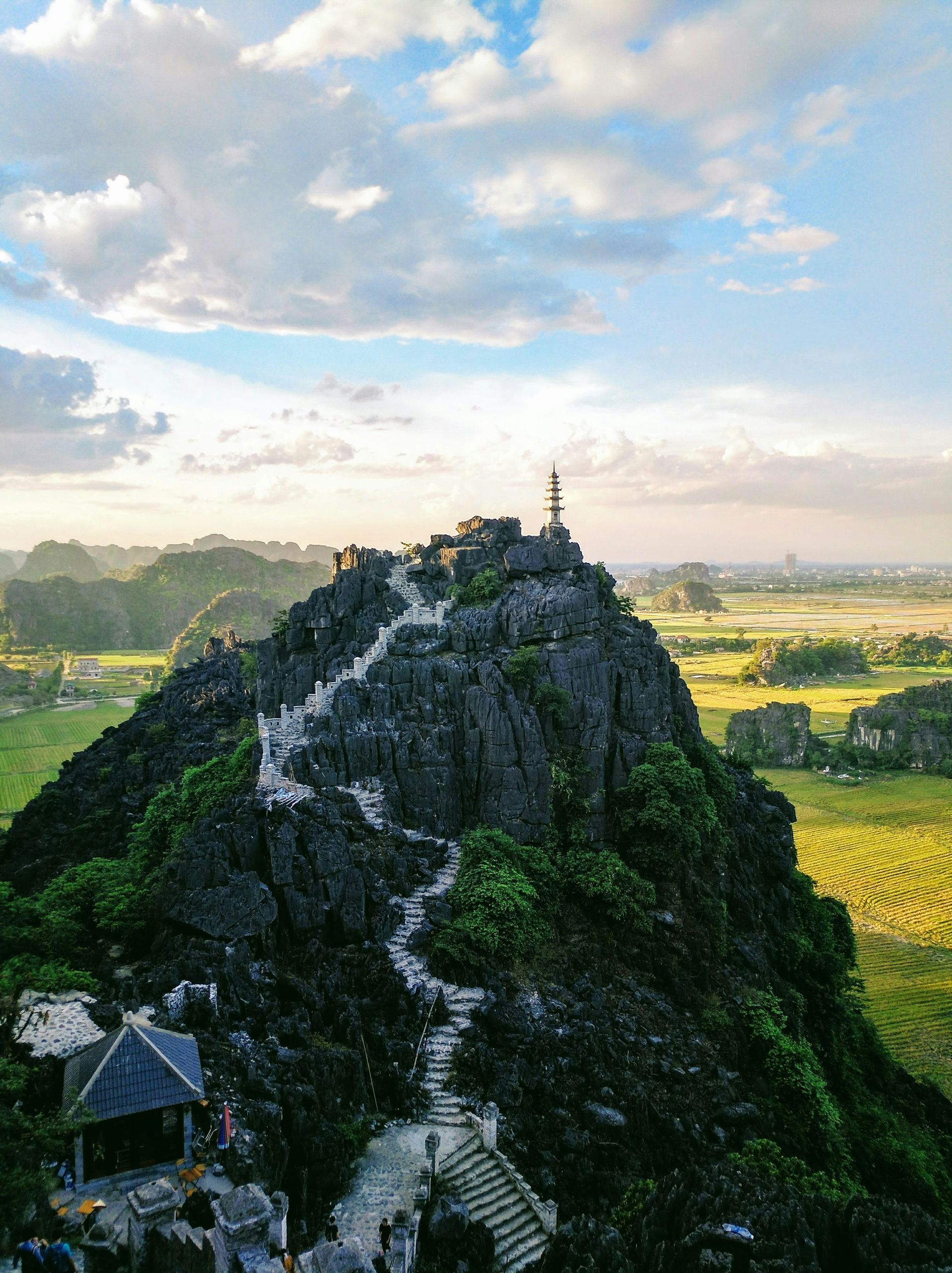 Staircase ascends a lush, rocky peak with a pagoda, overlooking a verdant valley in Ninh Bình, Vietnam.