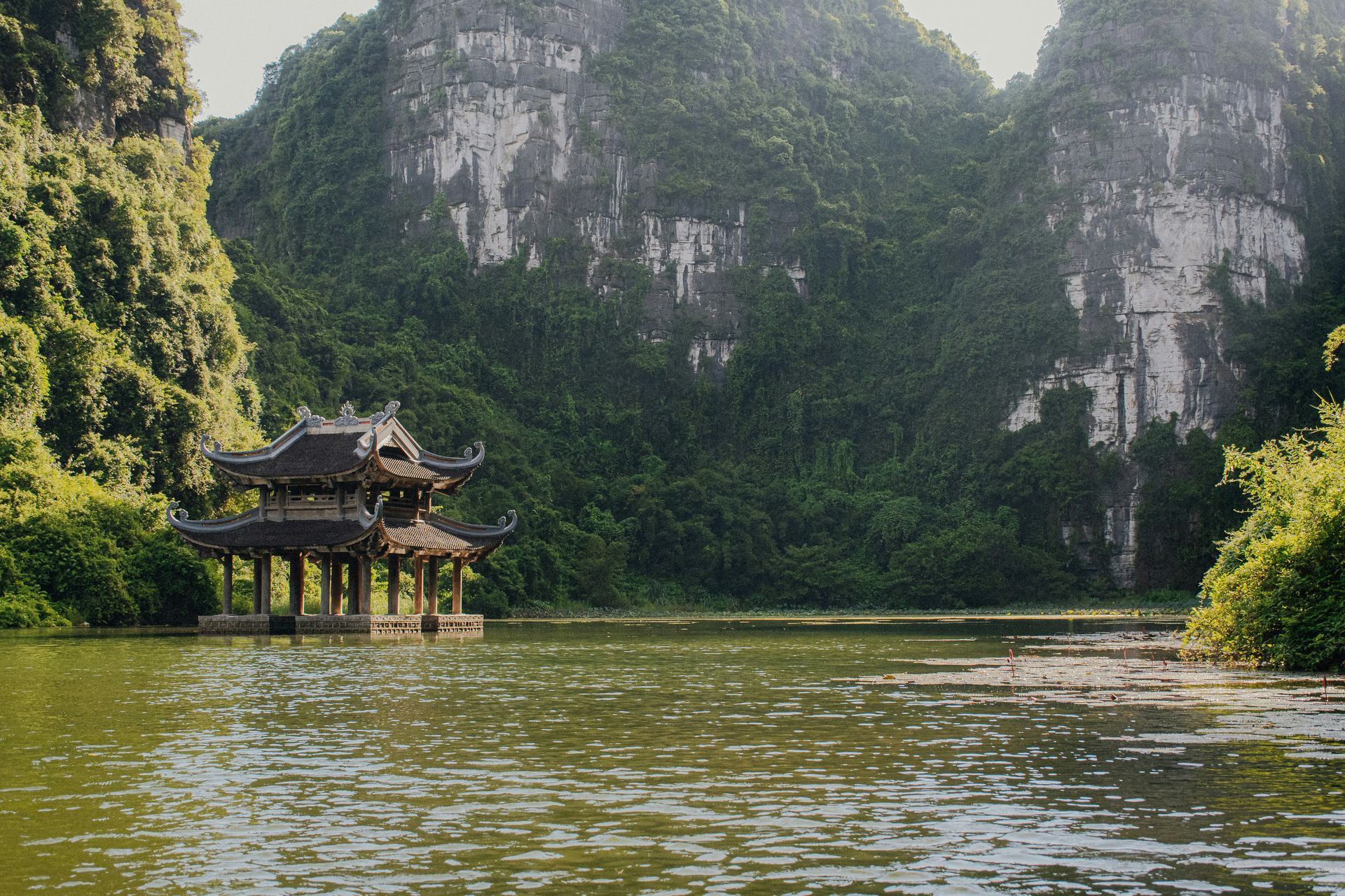 Pagoda on a lake surrounded by lush, green mountains in Ninh Bình, Vietnam.