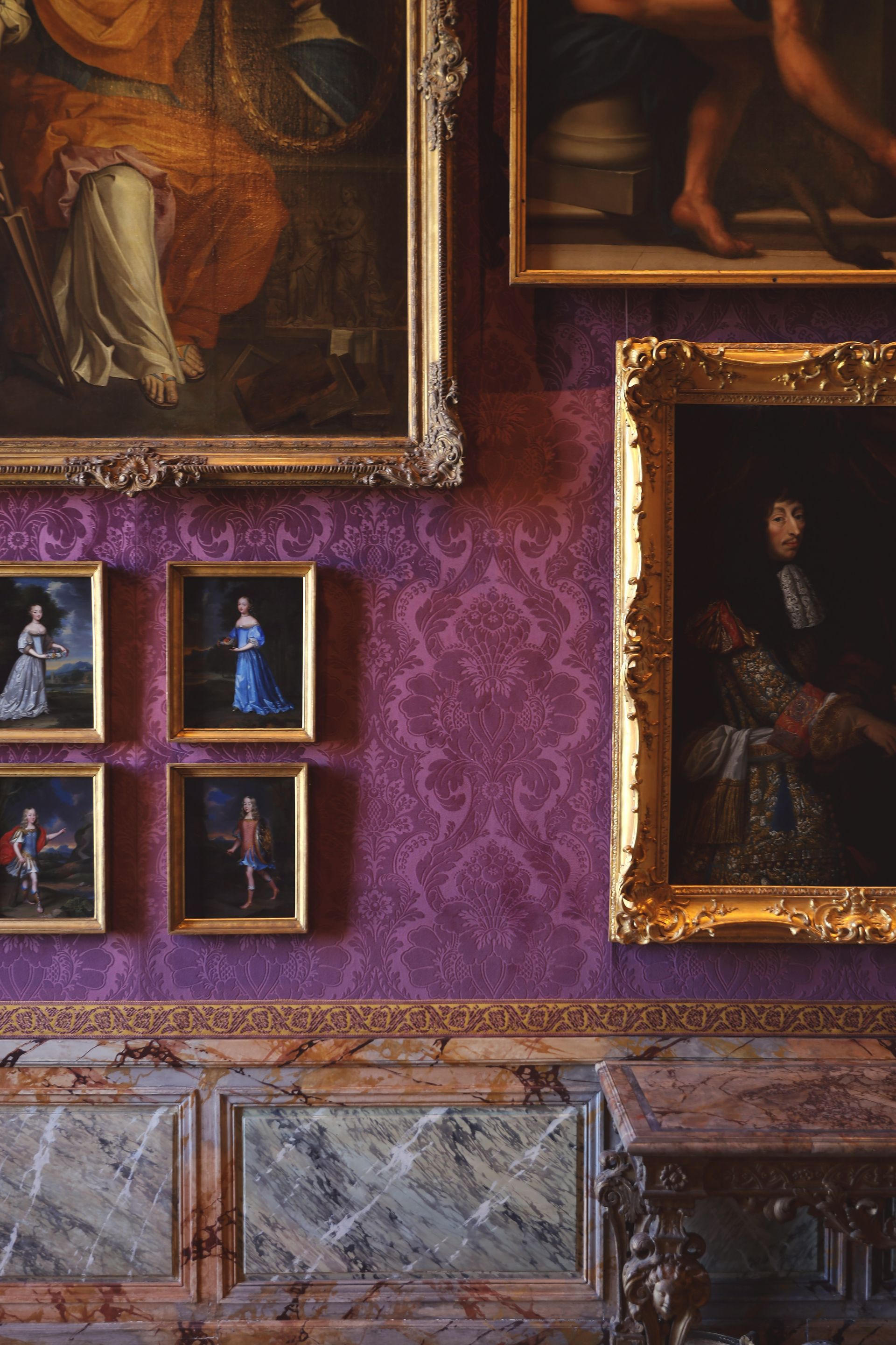 Several paintings are hanging on a purple wall at the Palace of Versailles in France.