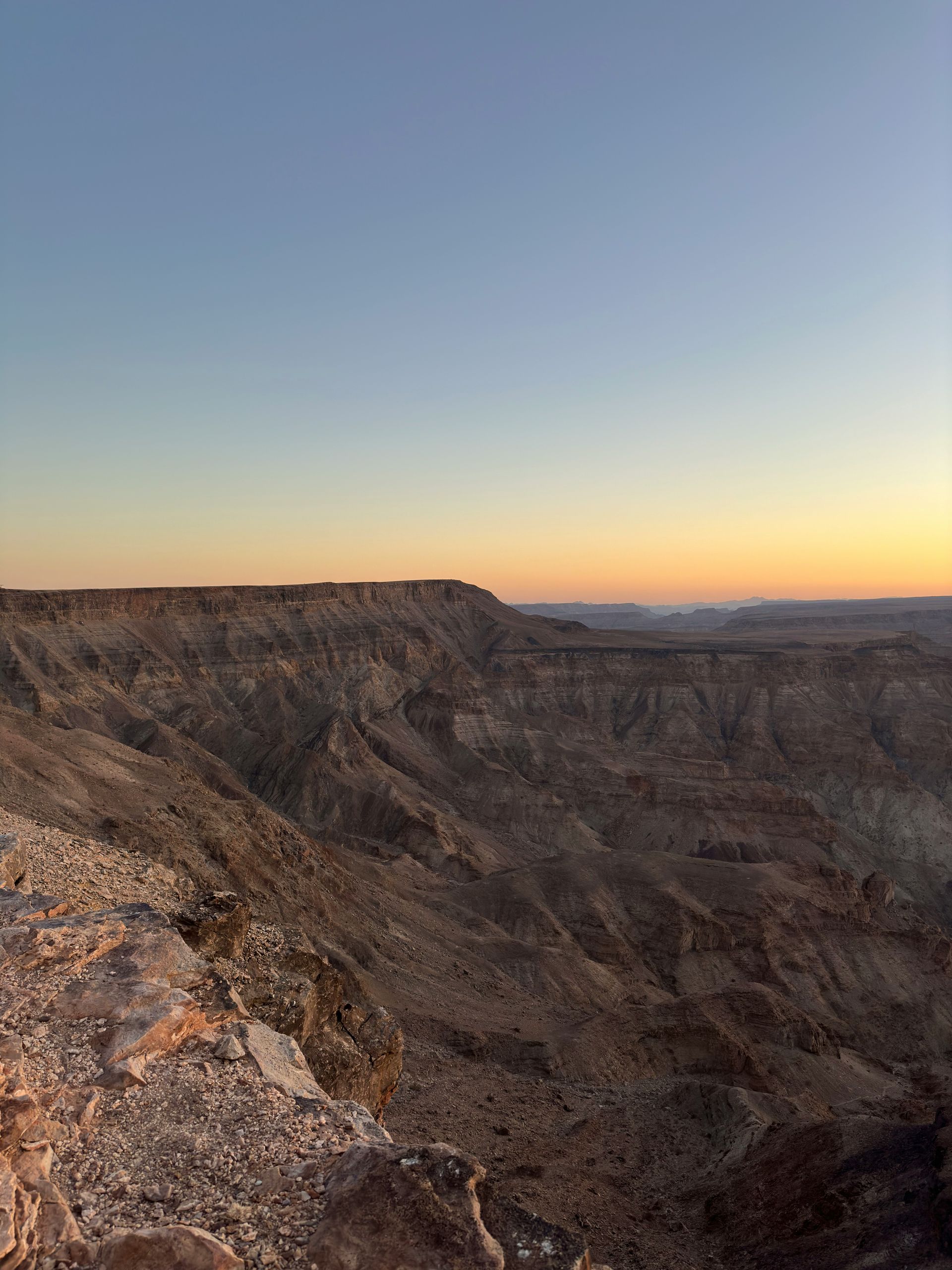 Fish River Canyon landscape at dusk with a gradient sky: blue to orange. Rugged terrain and a distant horizon.
