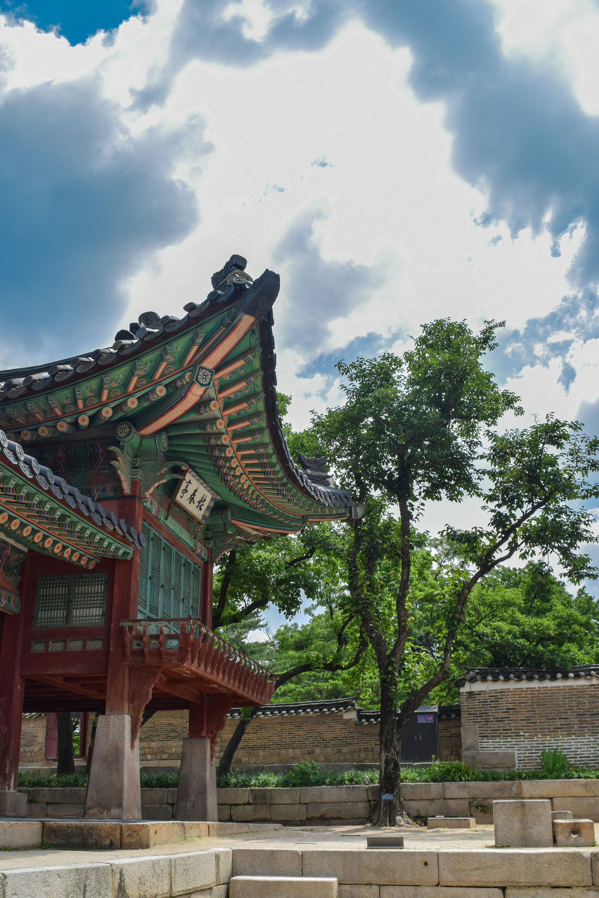 Changdeokgung Palace with colorful roof, stone pillars, and lush green trees in South Korea.