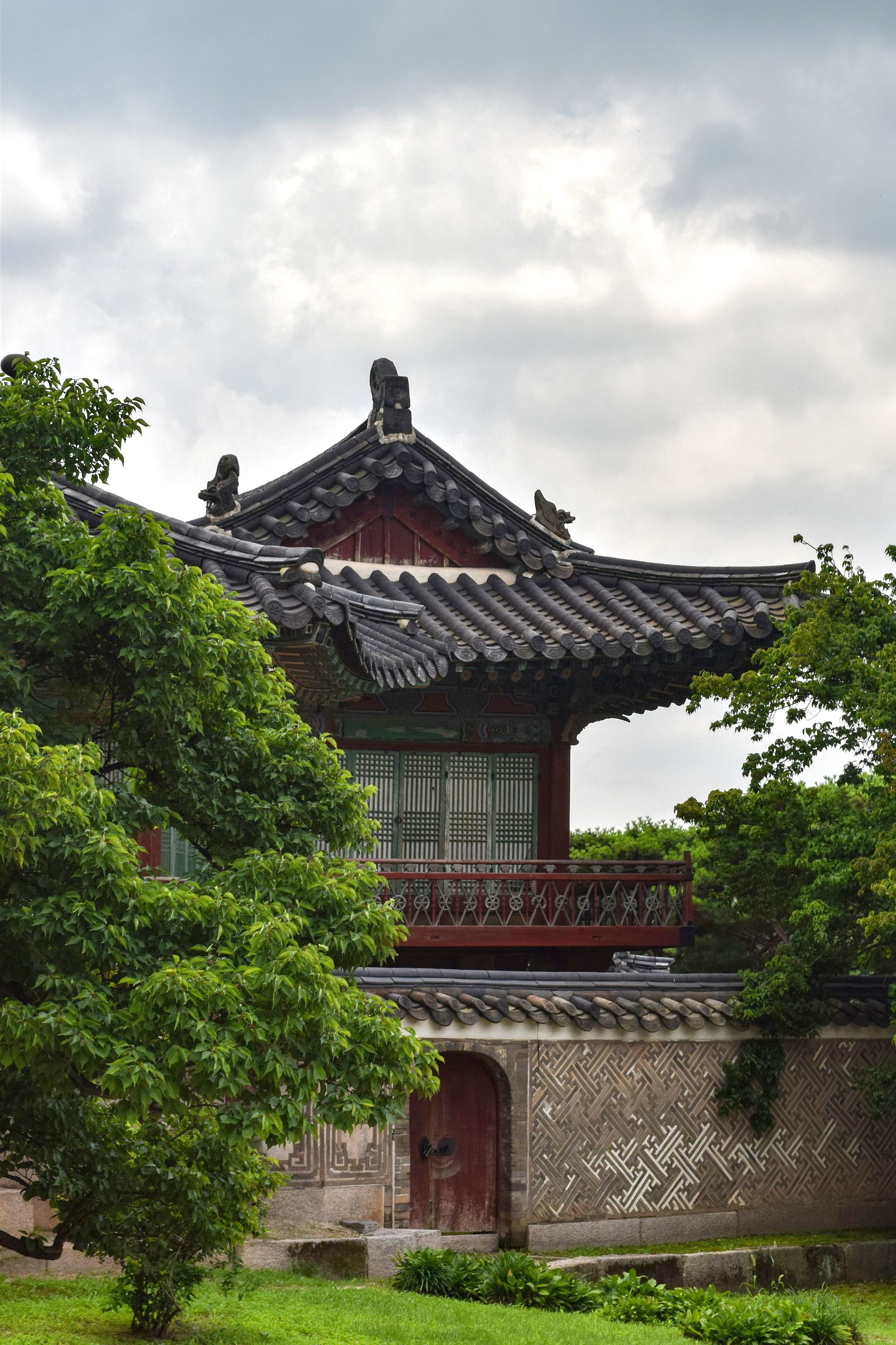 Changdeokgung Palace with tiled roof, red accents, and stone wall, viewed through trees in South Korea.