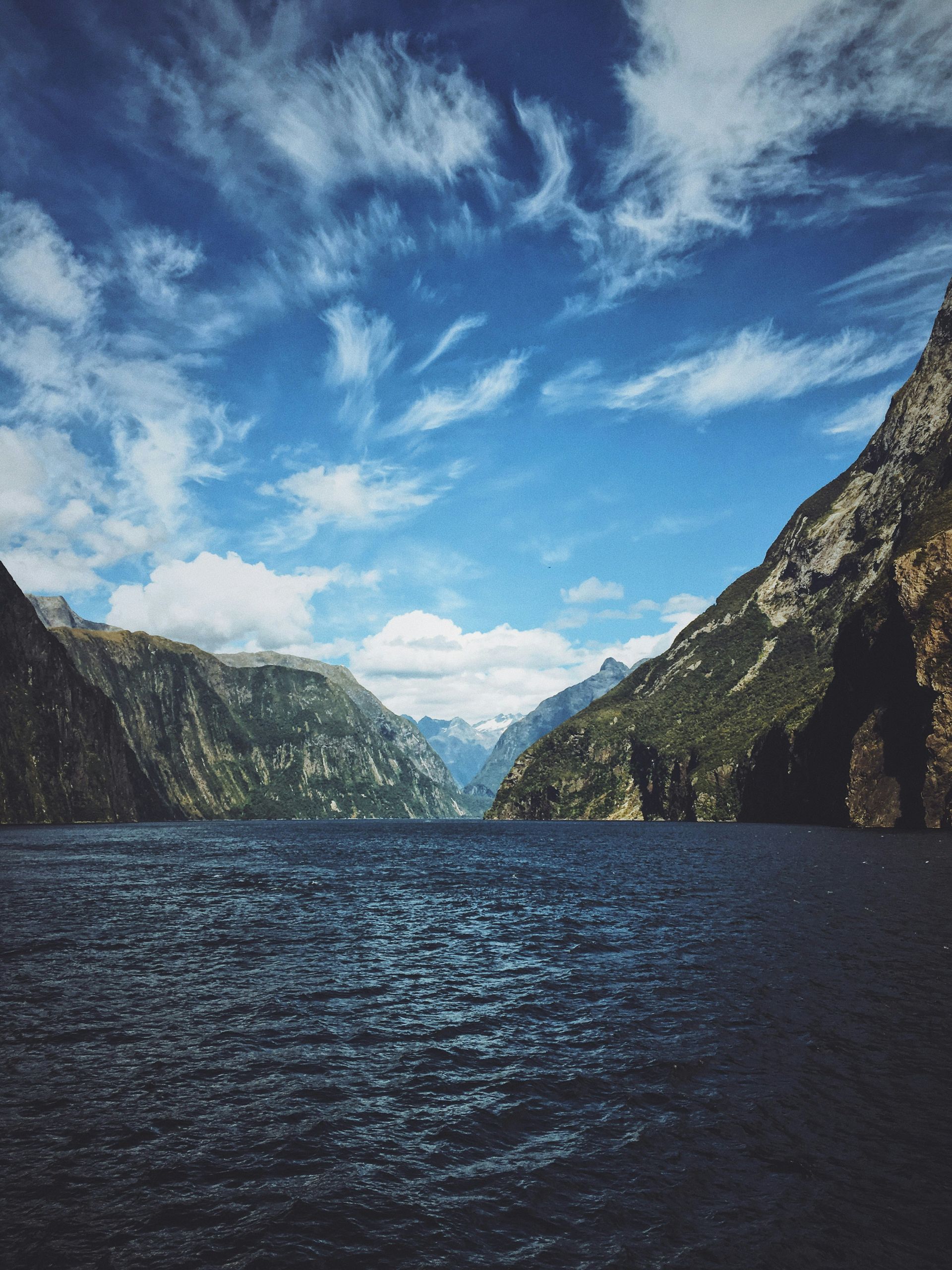 A fiord with mountains in the background and a blue sky in Fiordland National Park, New Zealand.
