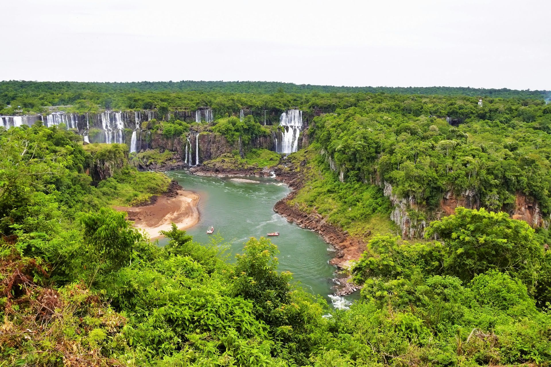 Lush green rainforest surrounds a river and numerous waterfalls cascading into the water at Iguazu Falls, Argentina.