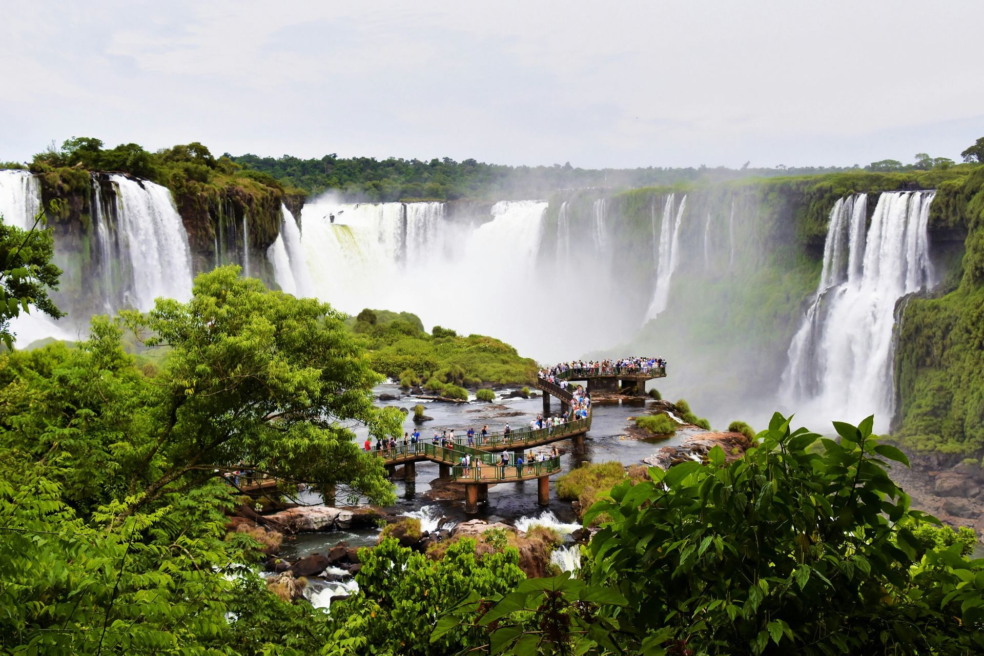 Iguazu Falls, Argentina. Several waterfalls cascade into a misty gorge, with lush green foliage and a viewing platform.