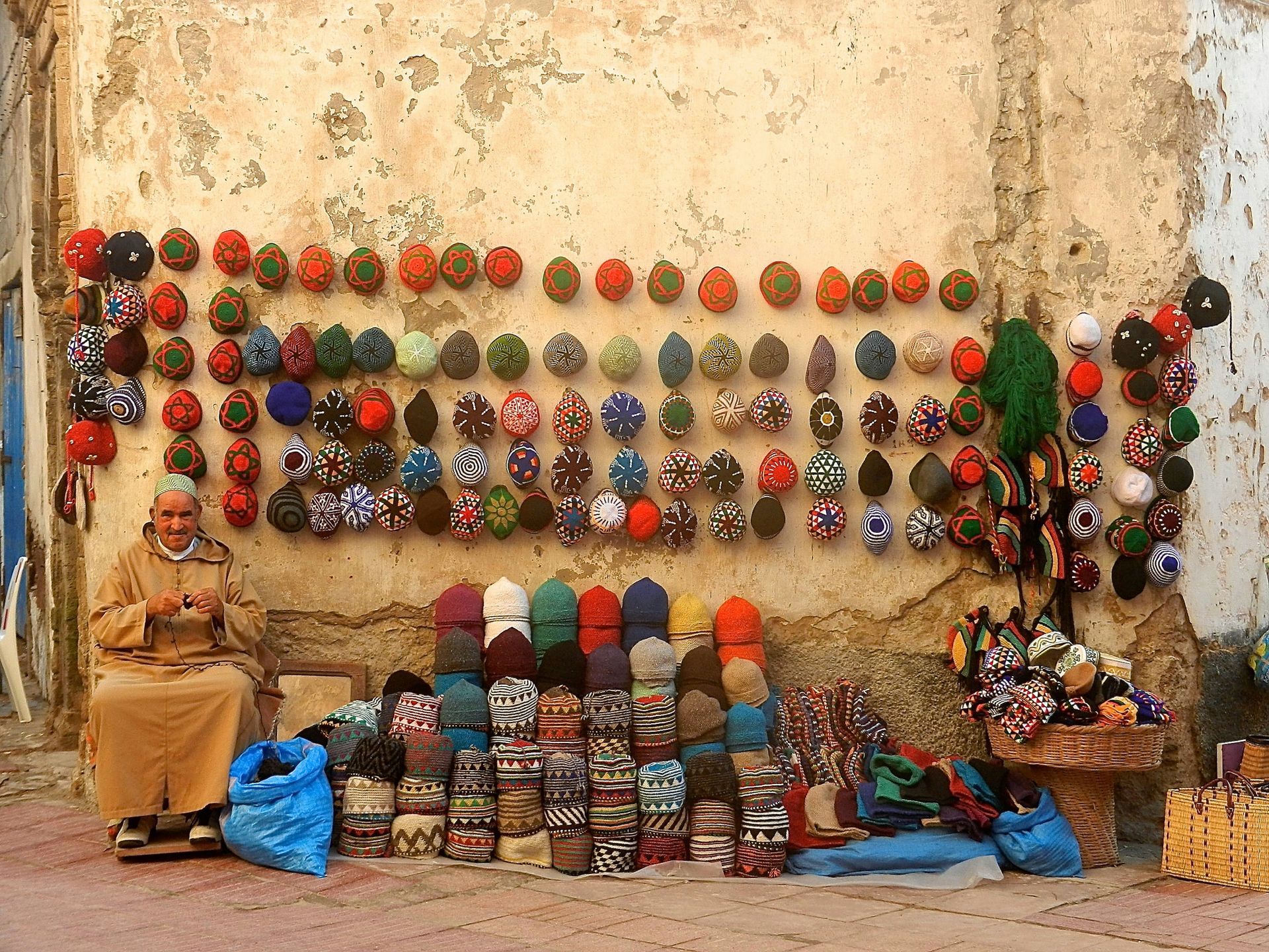A man sits in front of a wall full of hats in Essaouira, Morocco.