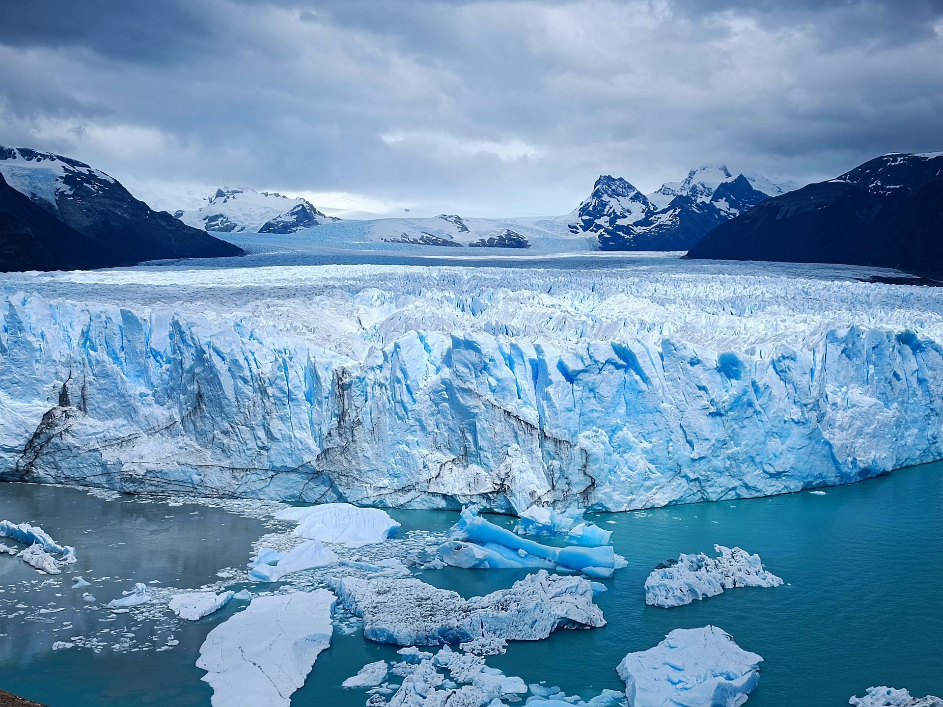 Glacier with ice chunks in water, mountains in the background at Parque Nacional Los Glaciares in El Calafate, Argentina.