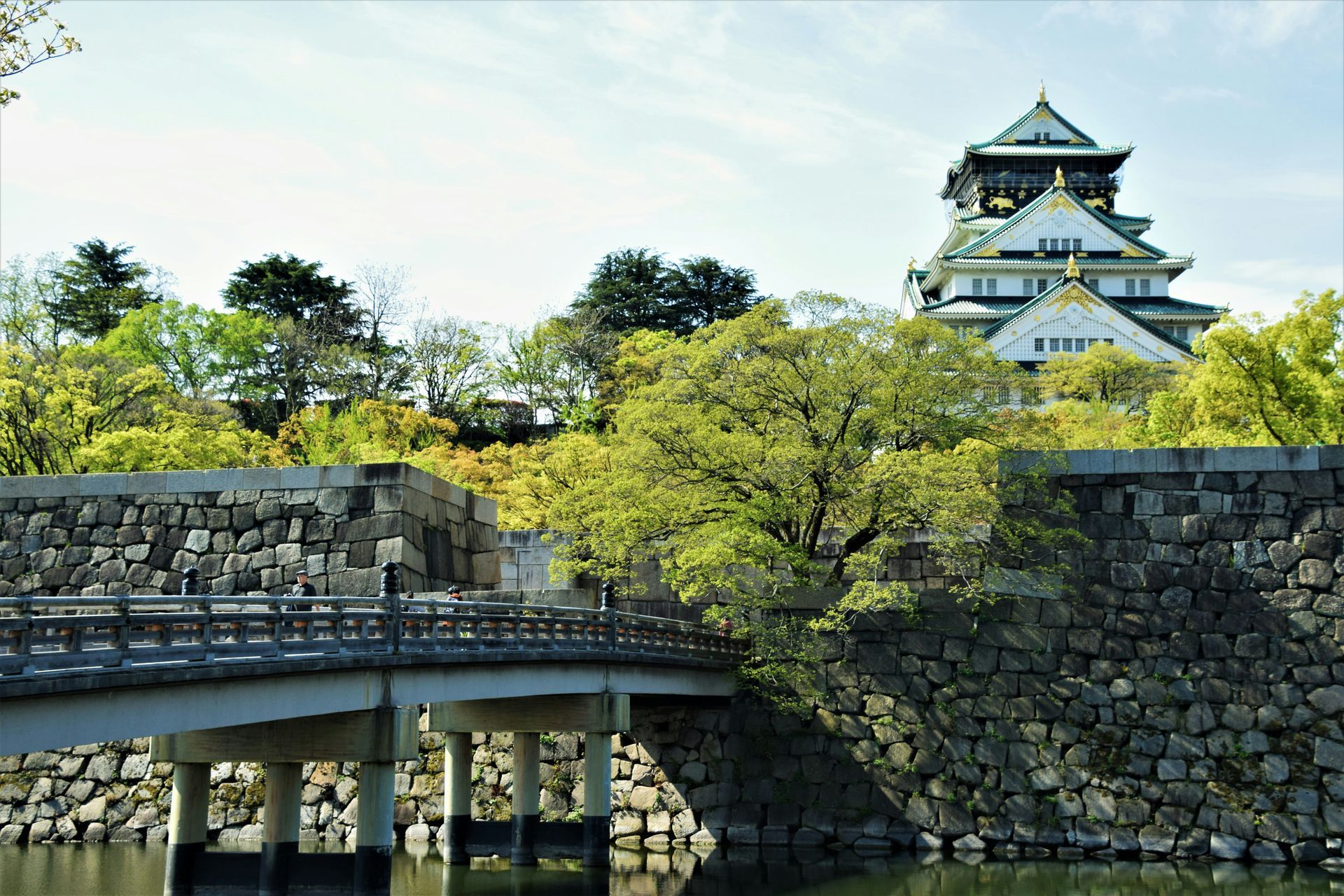 Osaka Castle, Japan, rises above a stone wall, bridge, and surrounding greenery.