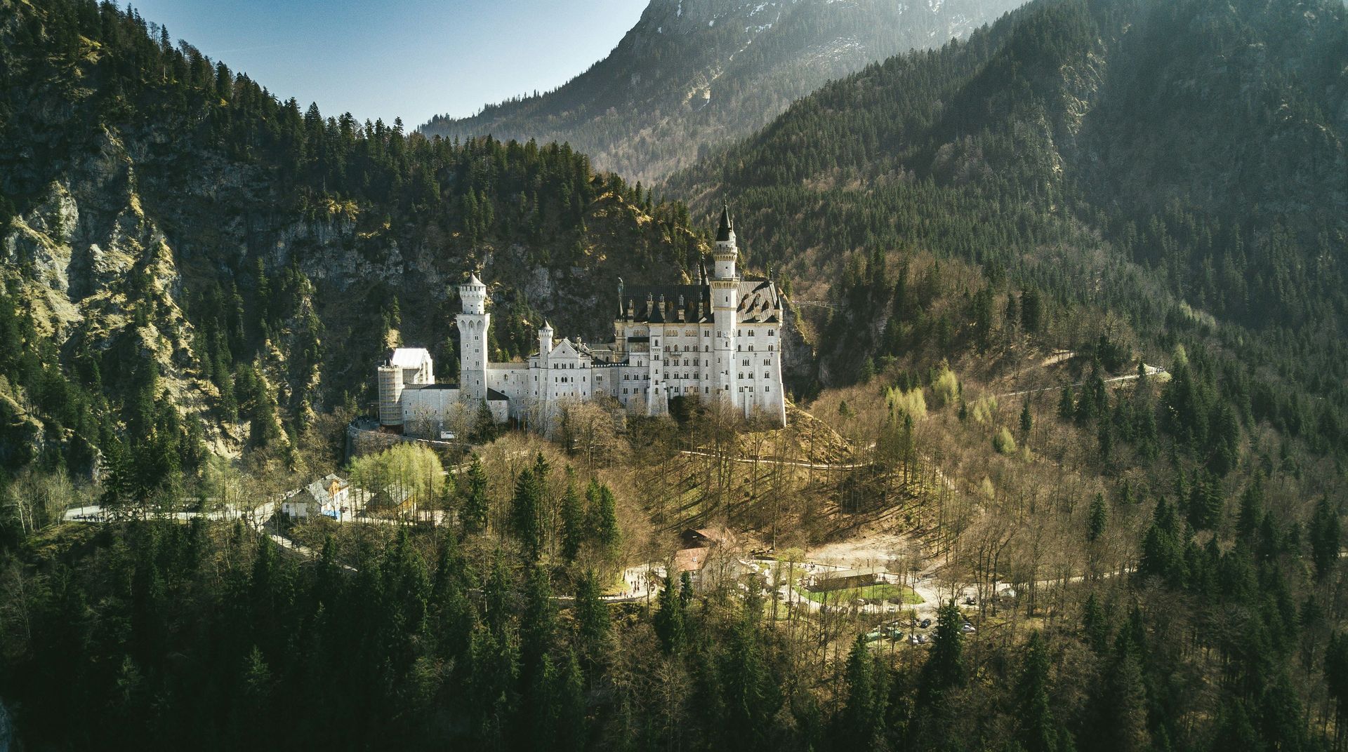Neuschwanstein Castle nestled in a green mountain landscape with snow-capped peaks.