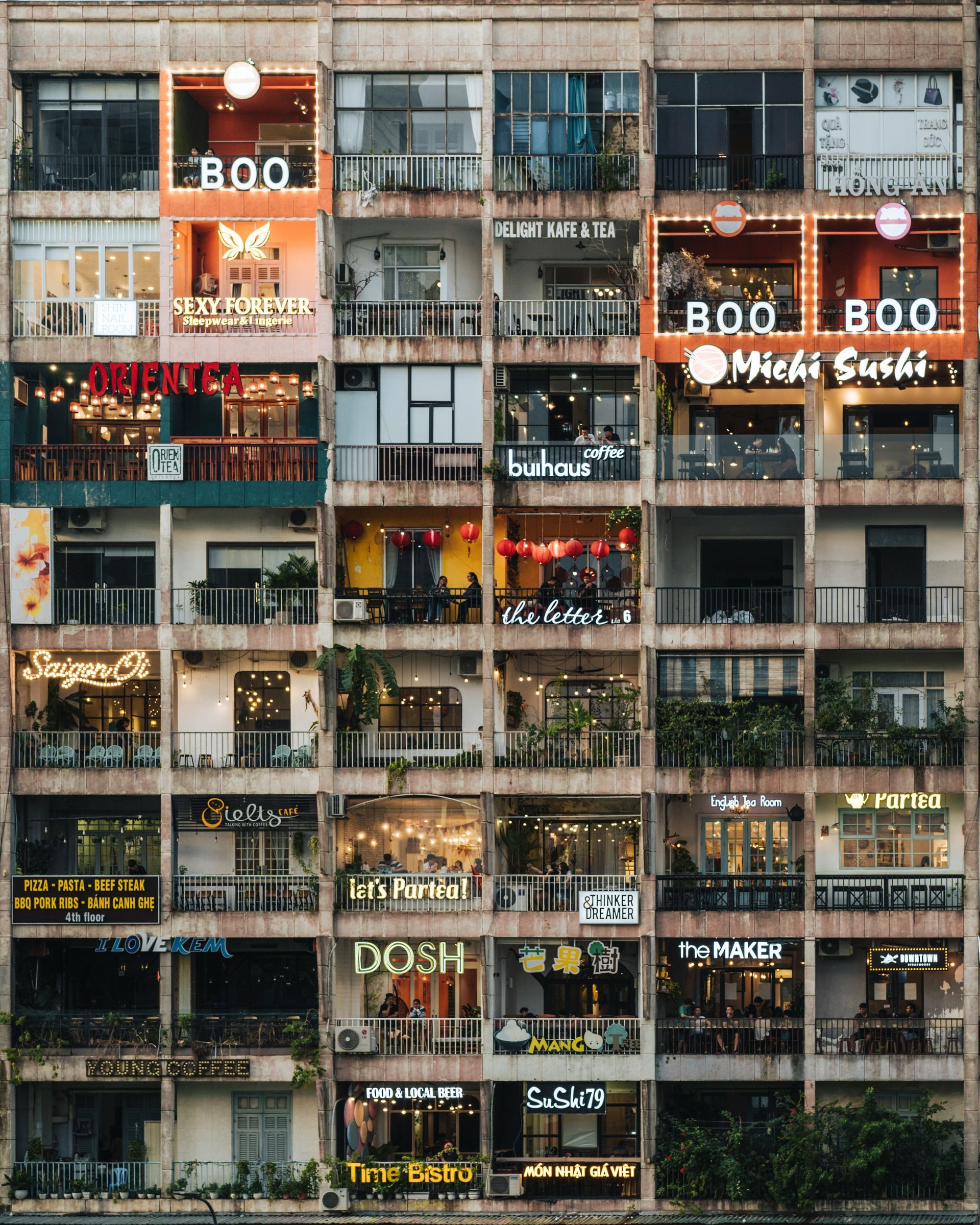 Multi-story building with many lit shop signs, cafes, and balconies in Ho Chi Minh, Vietnam.