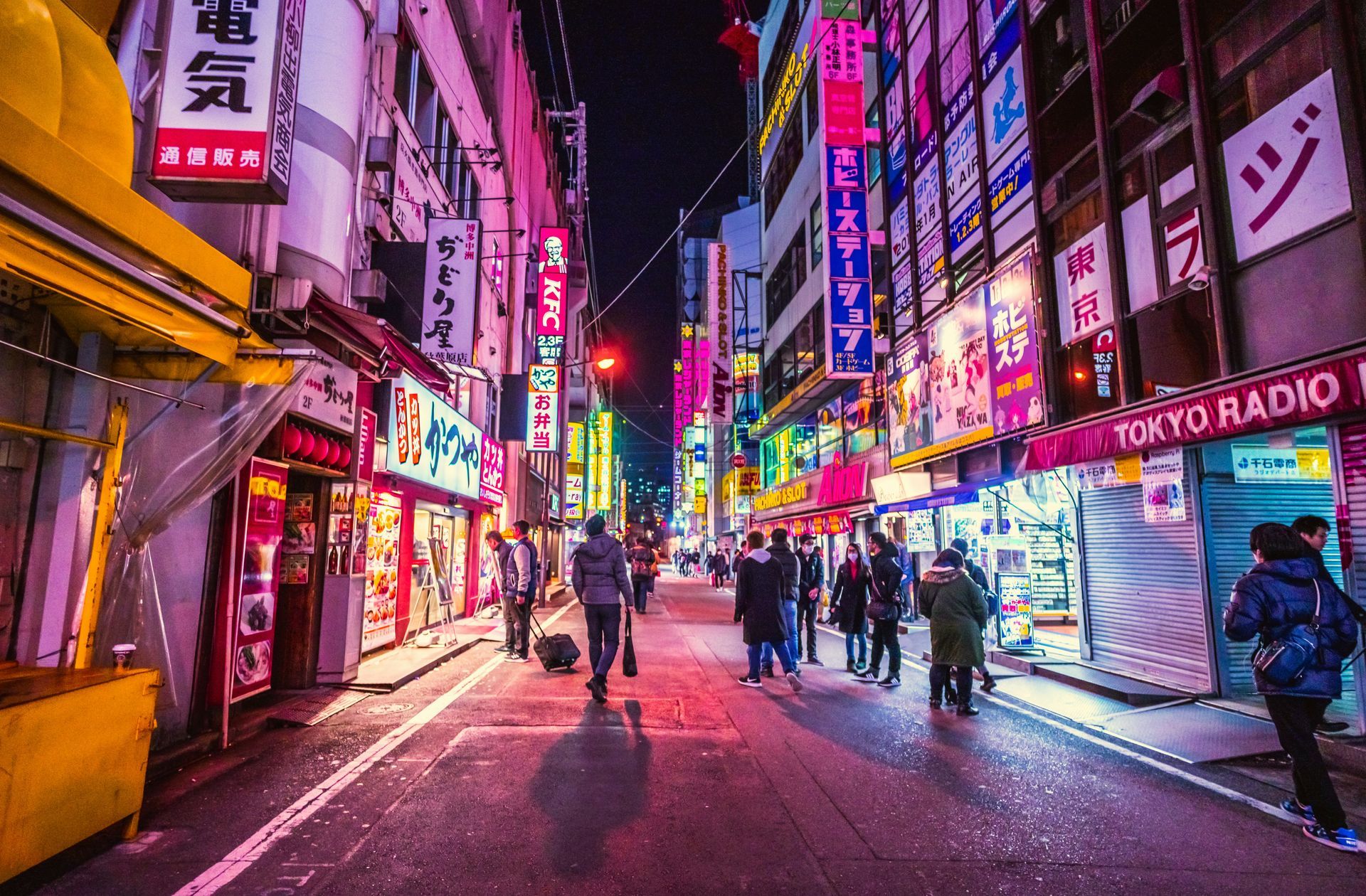 Neon-lit street in Tokyo at night, with storefronts, pedestrians, and colorful signs.