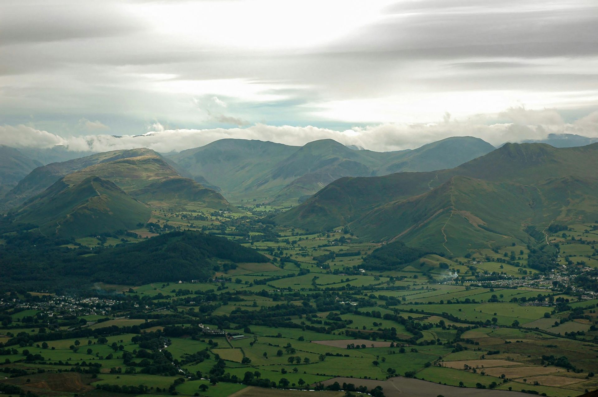 Green valley nestled between rugged mountains under a cloudy sky in the Lake District, England.