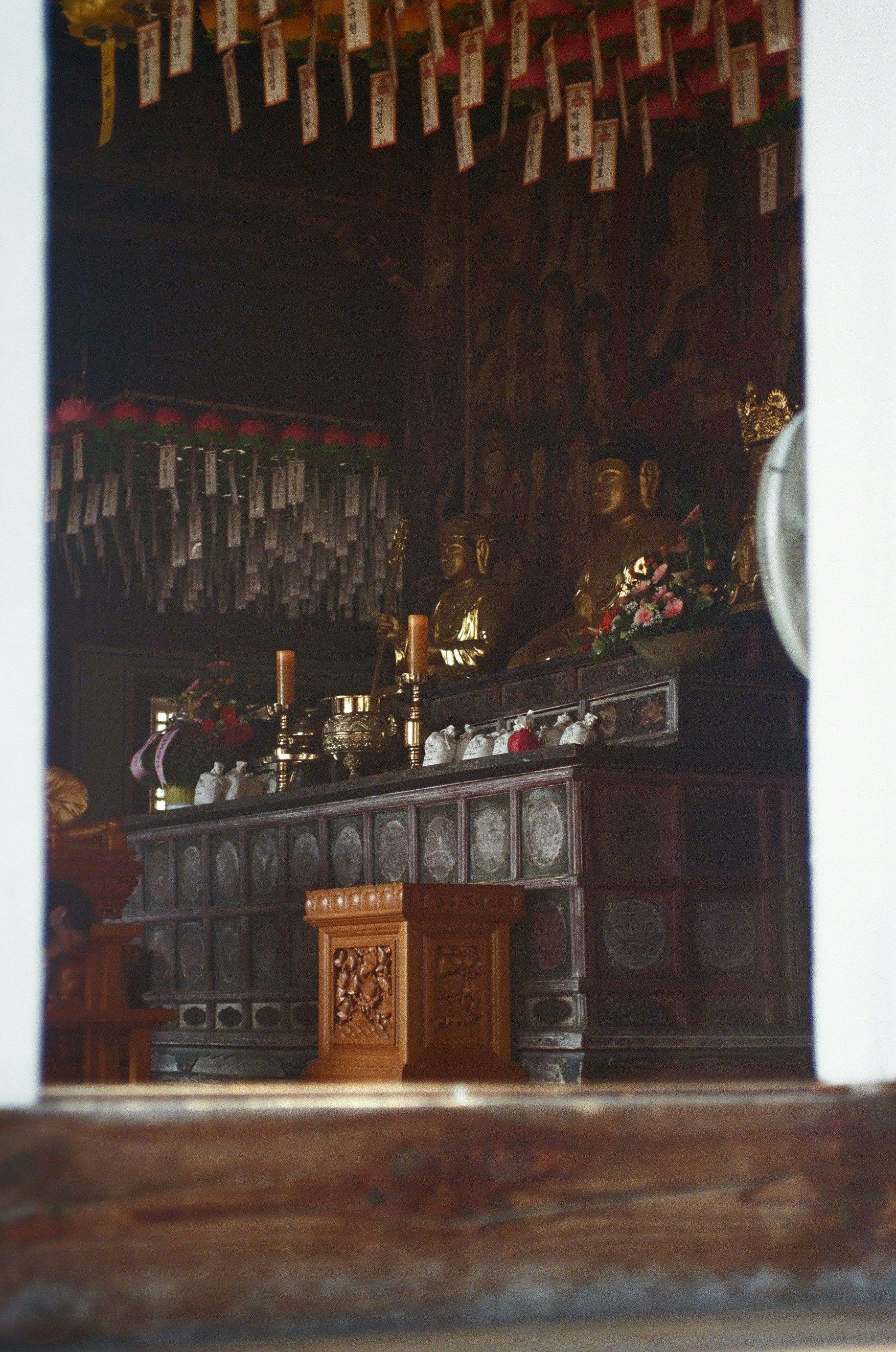 View through an opening into a dimly lit temple with altar, candles, and hanging paper tags in Andong Hahoe Folk Village.