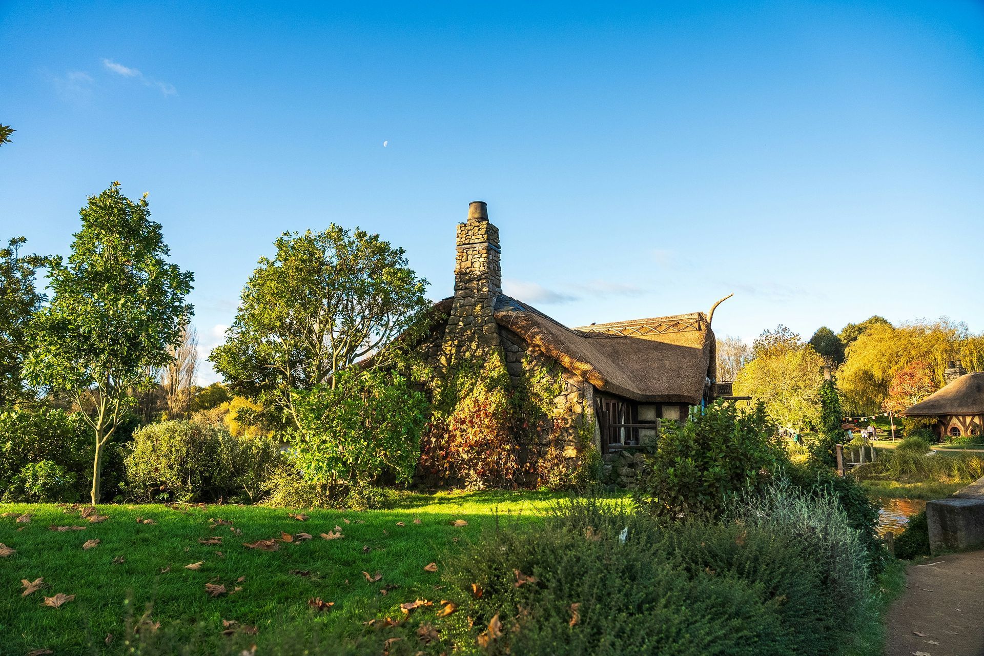 A cottage with a thatched roof is surrounded by trees in a park at the Hobbiton Movie Set in Matamata, New Zealand.