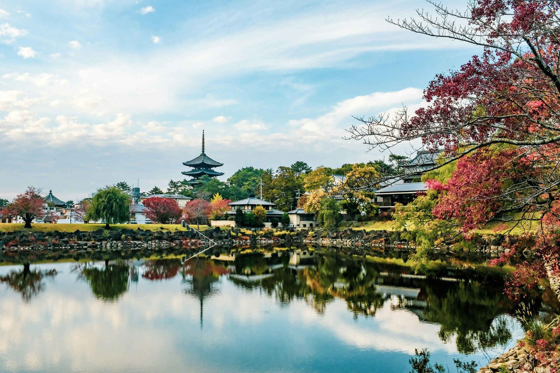 Scenic view of a lake reflecting a pagoda and autumn foliage in Nara, Japan.